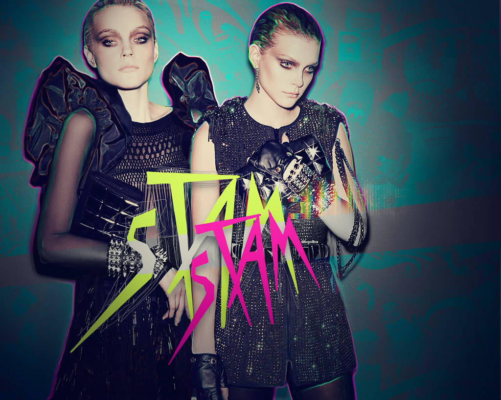 jessica stam 桌布 壁紙 — 兩位模特兒身穿前衛黑色服裝，在帶有粗體霓虹塗鴉文字的藍綠色背景前擺姿勢。