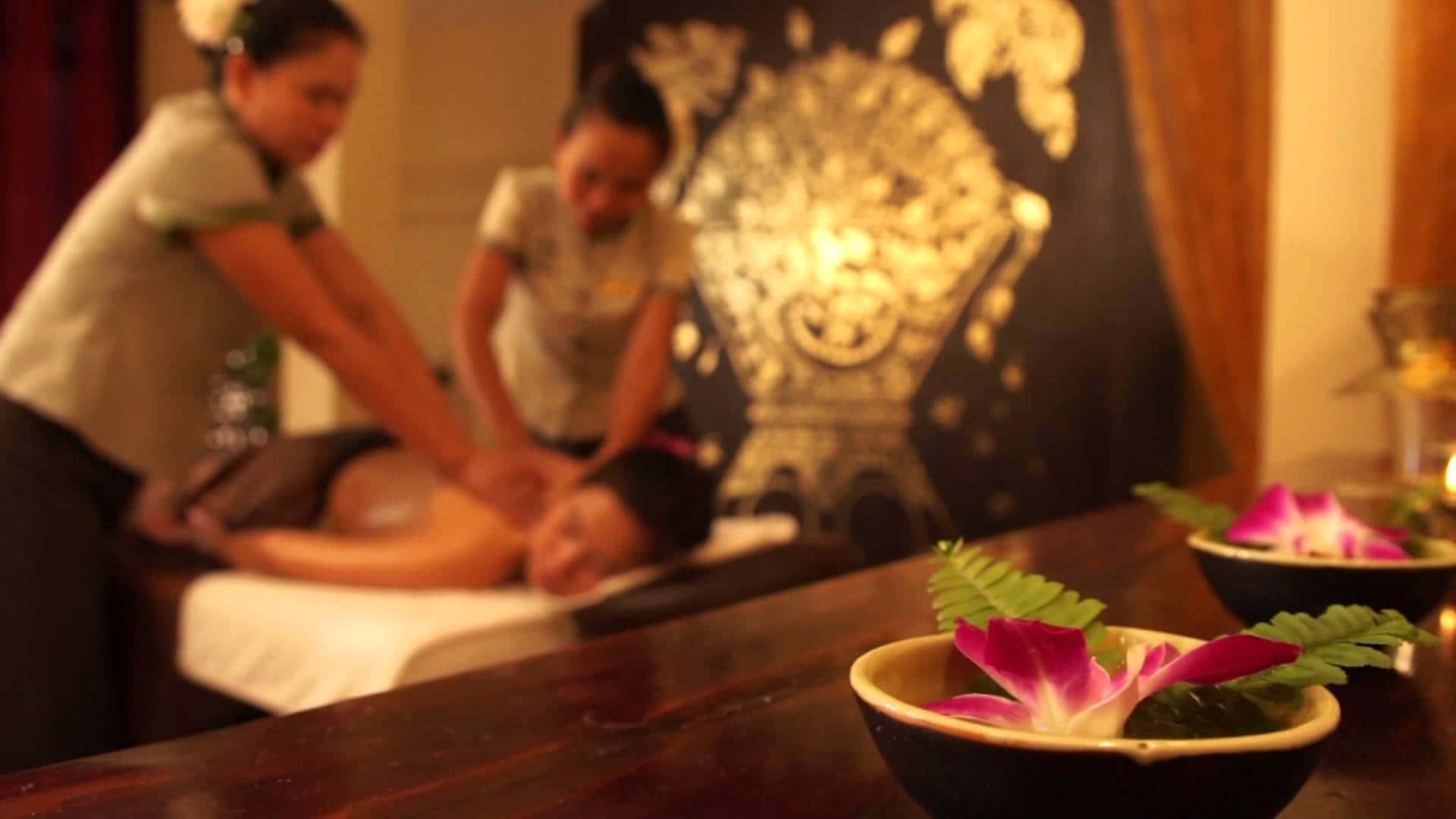 Massage 桌布 壁紙 — 兩位治療師在燈光溫暖的水療中心為客戶進行放鬆按摩，碗中擺放著蘭花。