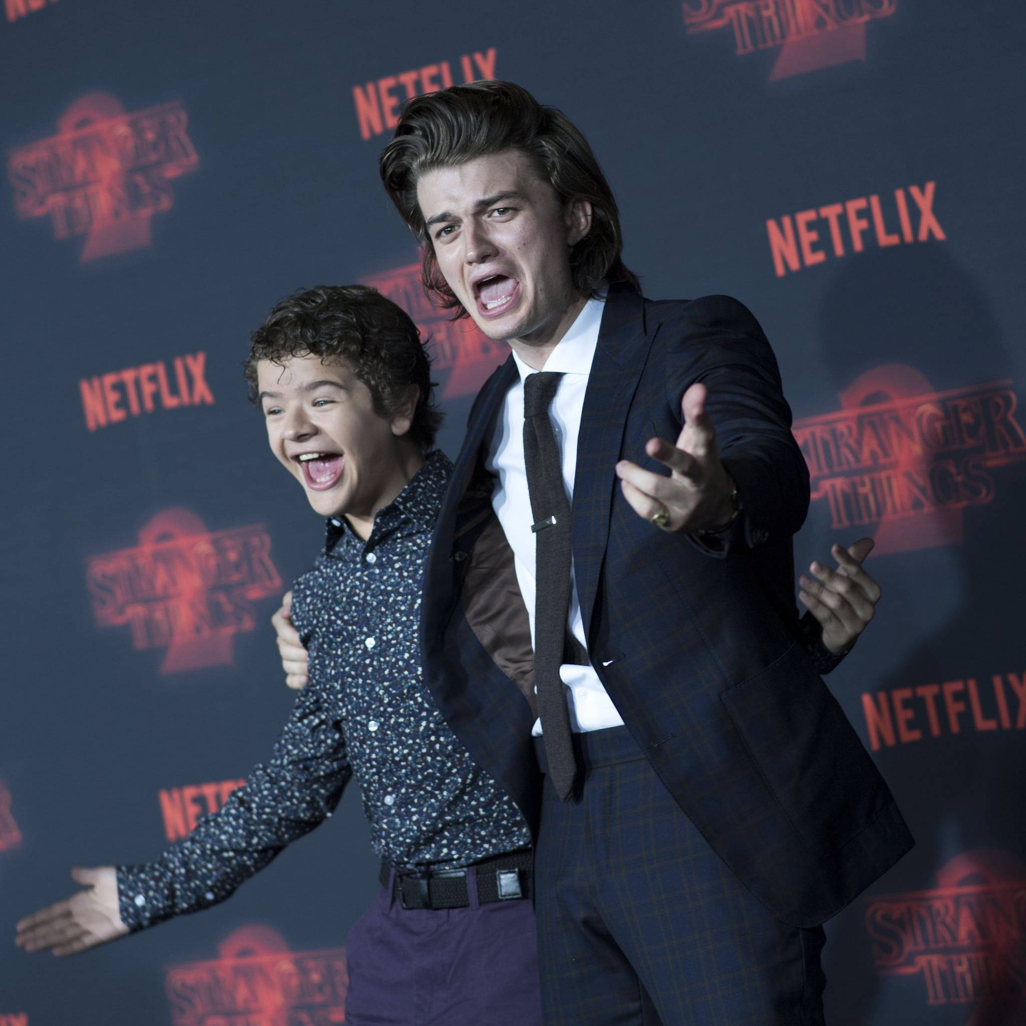 Joe Keery 桌布 壁紙 — 兩位演員穿著《怪奇物語》服裝，在Netflix活動中對著品牌背景充滿活力地擺姿勢。