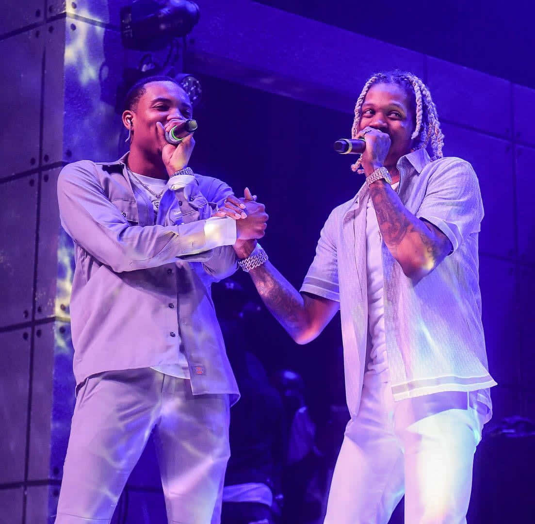 Herbo iPhone 桌布 壁紙 — 兩位男饒舌歌手在紫色燈光下於舞台上表演，手持麥克風並緊握雙手。