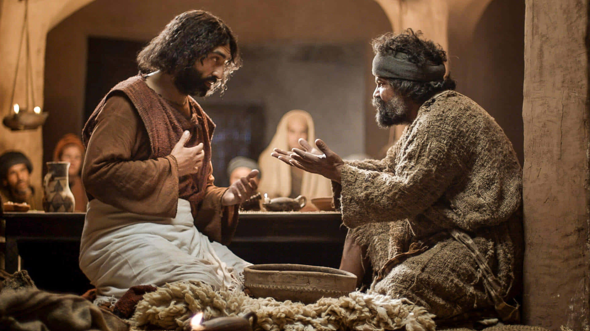 Jesus Disciples 桌布 壁紙 — 兩位留鬍鬚的男子身穿古裝長袍，在光線昏暗的石室中激烈交談，背景有其他人。