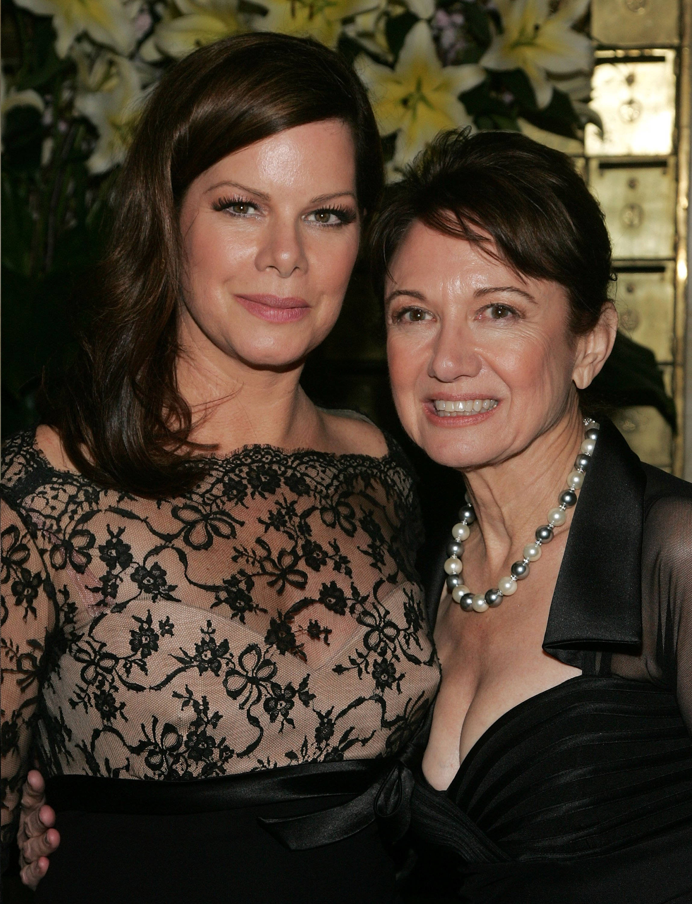 Celebrity 桌布 壁紙 — 兩位穿著優雅的女士在白色百合花和金色裝飾的背景旁溫暖地微笑。