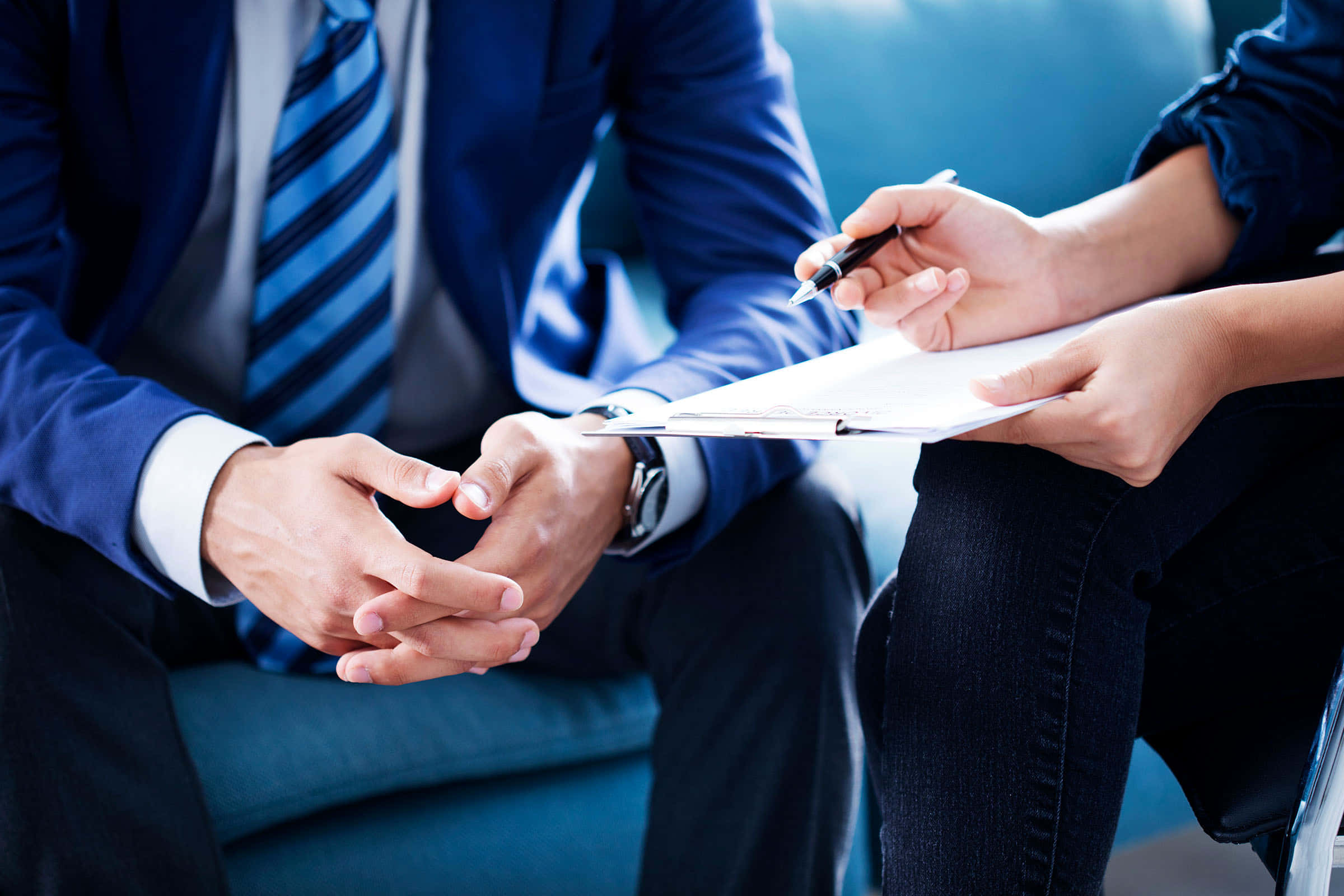 Business 桌布 壁紙 — 兩位穿著商務服裝的專業人士面對面坐著，一人拿著剪貼板和筆，另一人在專注的會議中雙手合十。