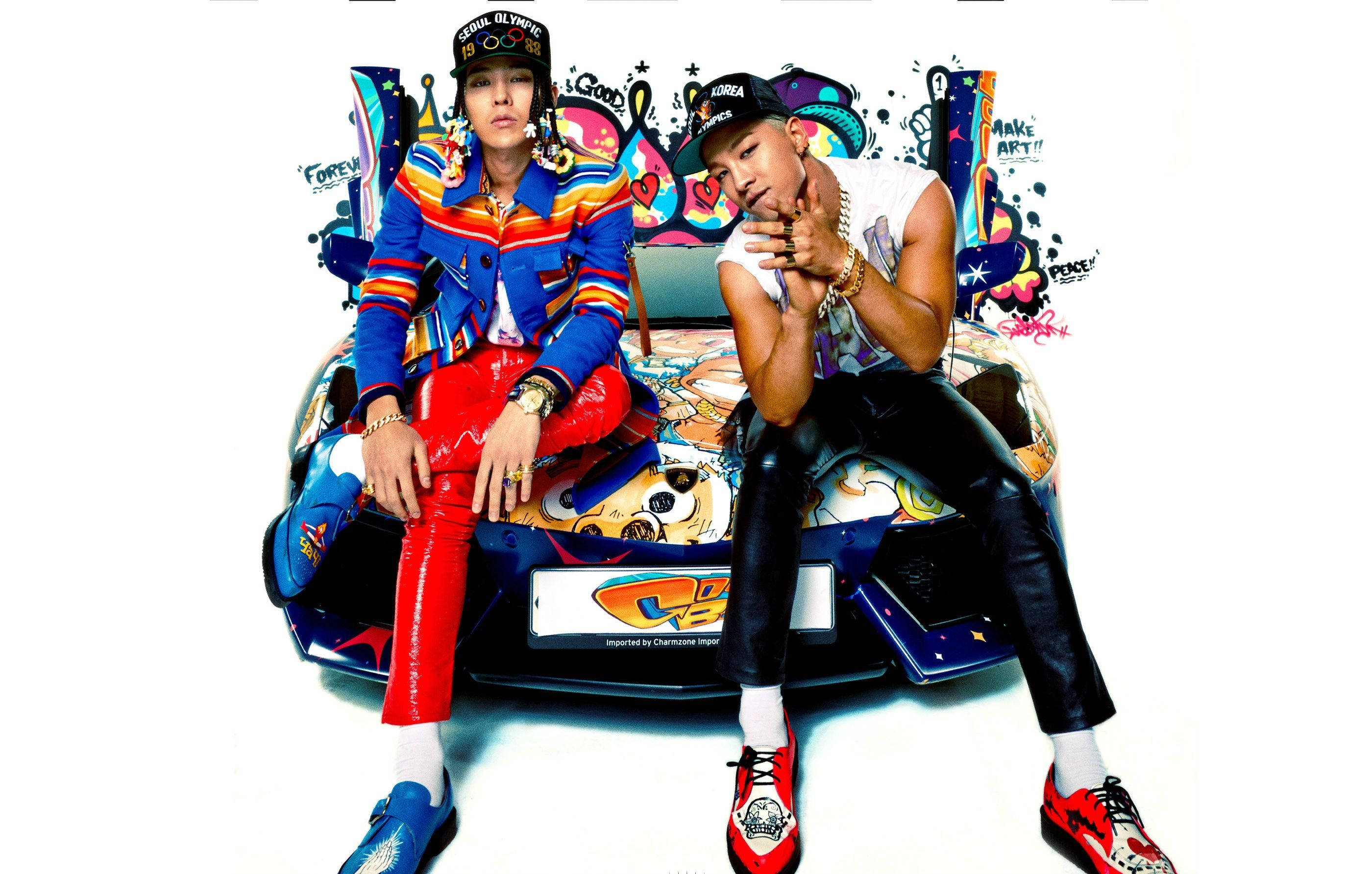 Bigbang 桌布 壁紙 — 兩位穿著時尚的男士自信地在一輛塗滿塗鴉的汽車上擺姿勢，背景是純白色。