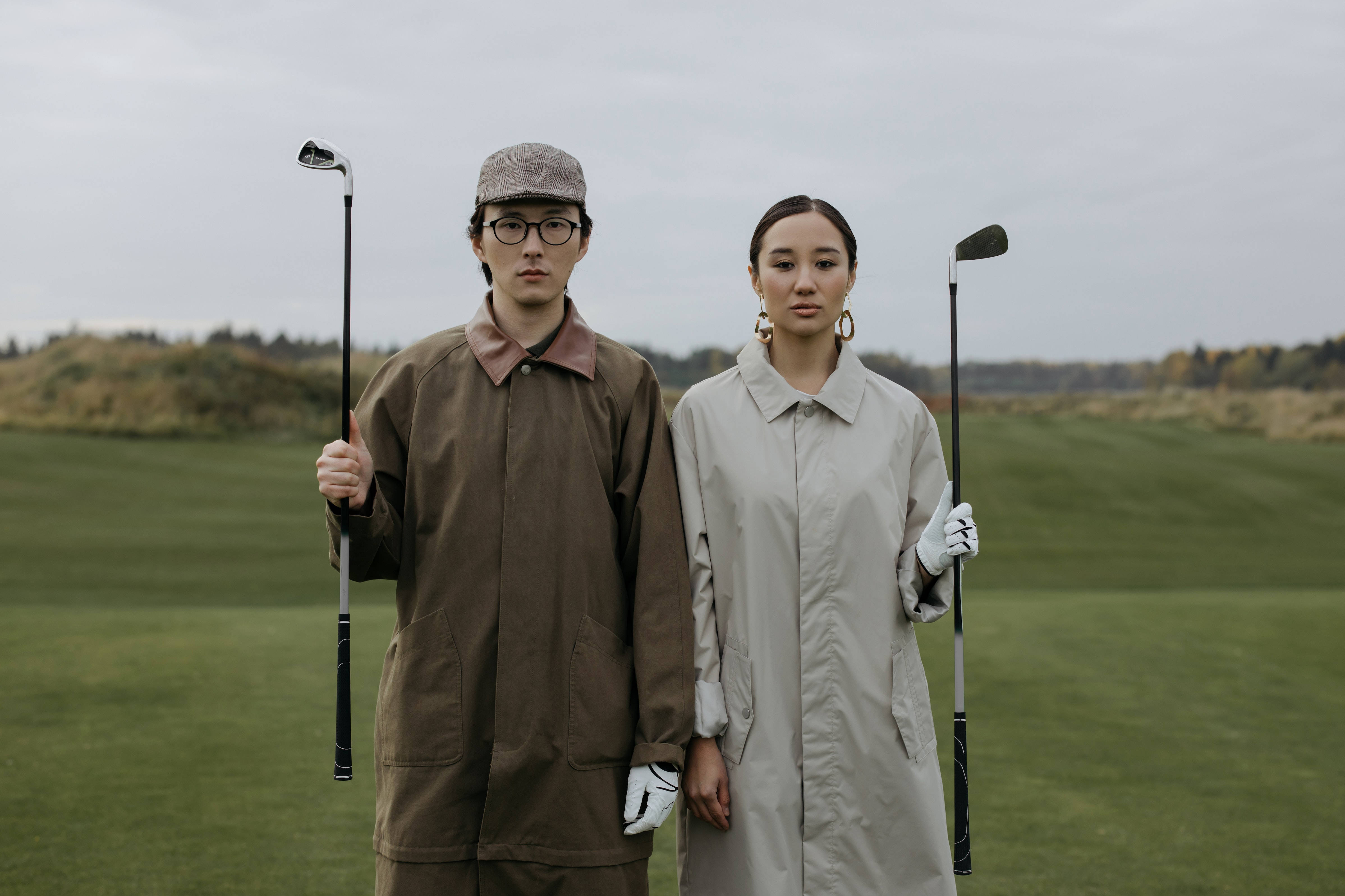 4K Golf 桌布 壁紙 — 兩位穿著時尚的高爾夫球手站在鬱鬱蔥蔥的球場上，在陰天手持球桿。