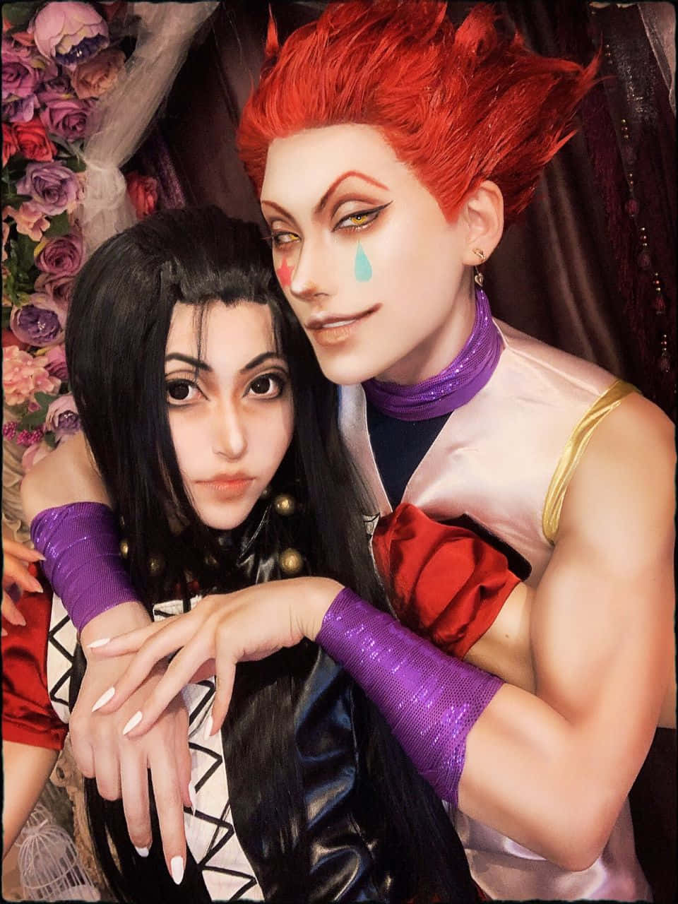 西索 桌布 壁紙 — 兩位穿著鮮豔動漫服裝的cosplayer在茂密的紫色和粉紅色玫瑰背景下親密擺姿勢。