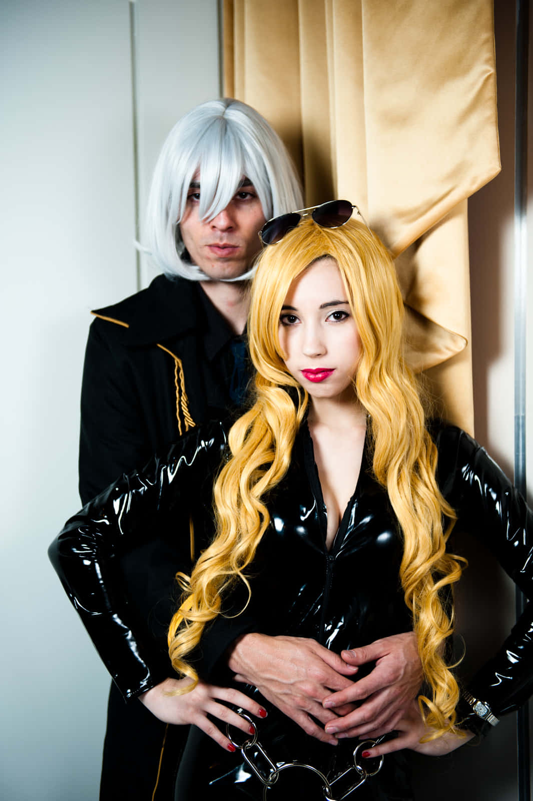 Cowboy Bebop Vicious 桌布 壁紙 — 兩位穿著黑色乳膠服裝的角色扮演者在米色窗簾前戲劇性地擺姿勢，一隻手放在對方的腰上。