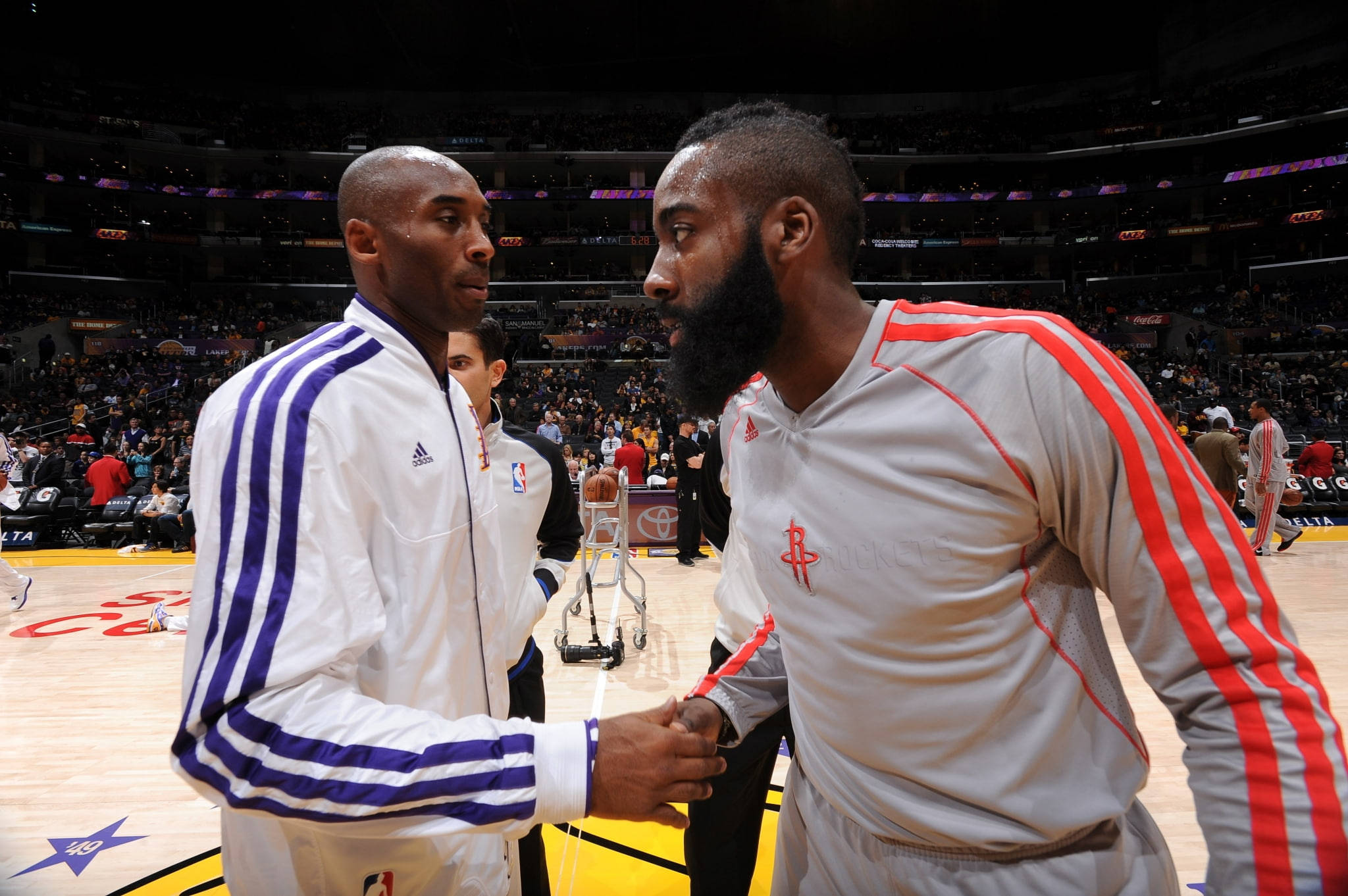 James Harden 桌布 壁紙 — 兩位籃球傳奇人物在燈光明亮的球場上握手，周圍是擠滿體育館的歡呼球迷。