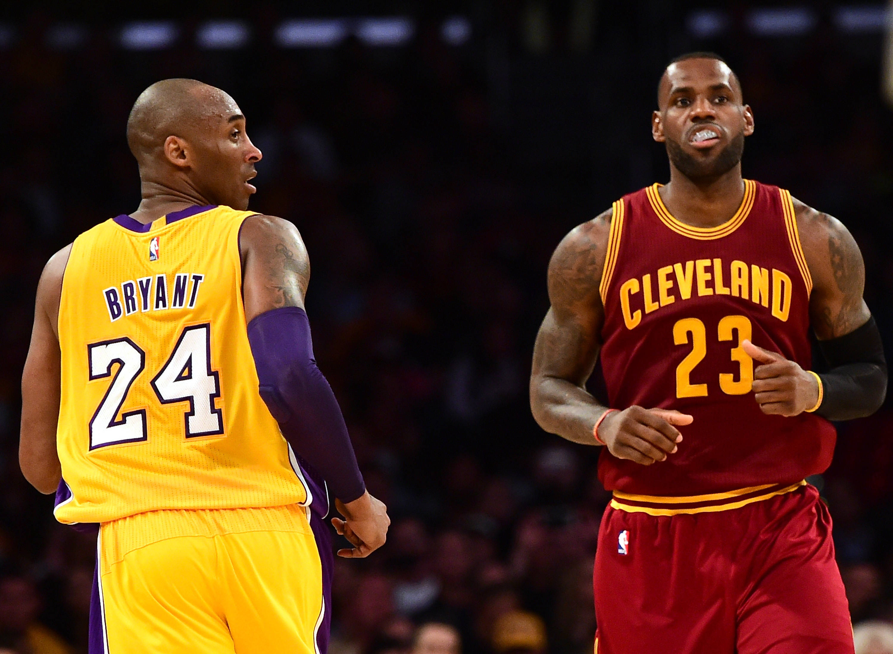 NBA 桌布 壁紙 — 兩位籃球傳奇人物柯比·布萊恩和勒布朗·詹姆斯在場館燈光下進行激烈的比賽對決。