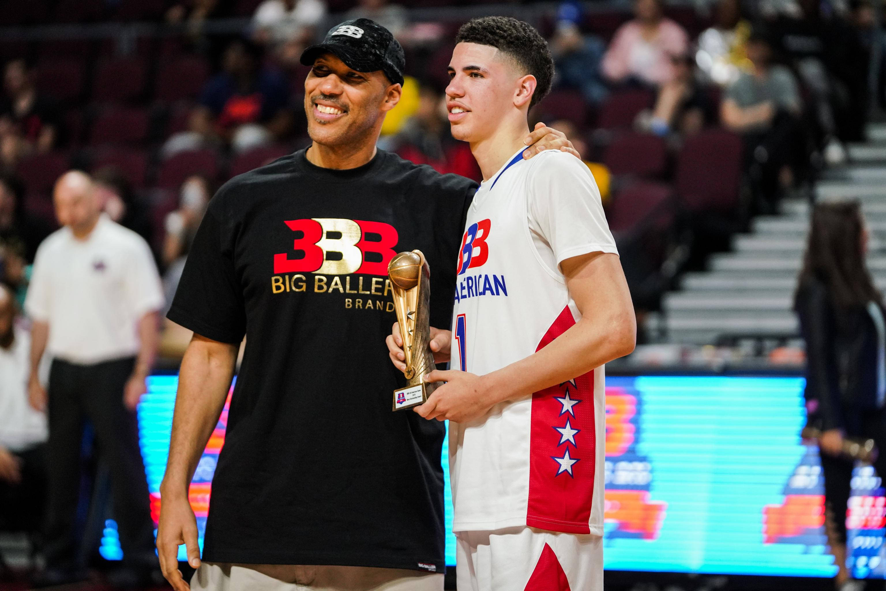 ball 桌布 壁紙 — 兩位籃球運動員一起微笑，其中一人手持獎盃，在燈光明亮的球場上，背景有球迷。