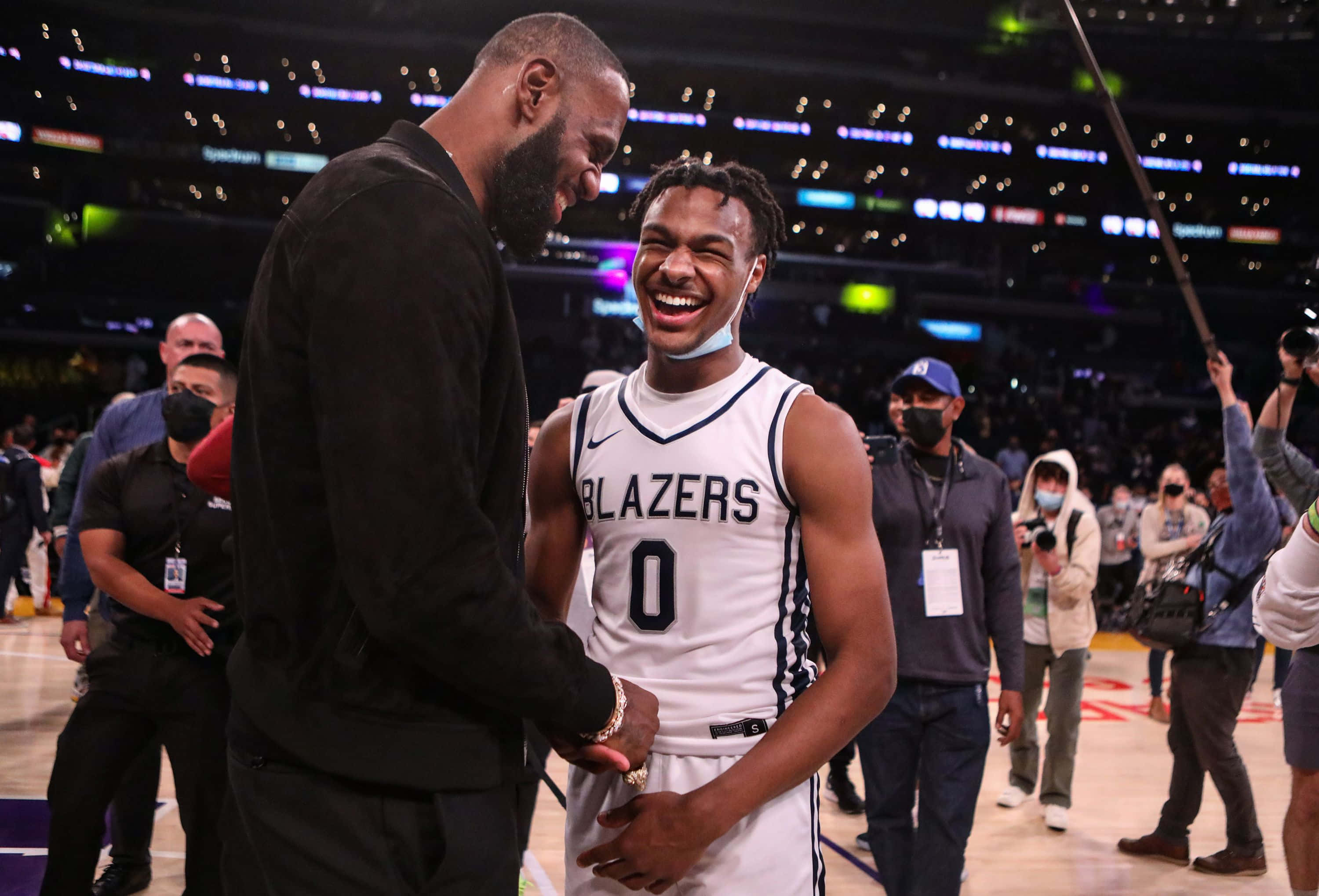 Bronny James 桌布 壁紙 — 兩位籃球運動員在燈光明亮的球場上愉快地握手，背景有球迷和攝影師。