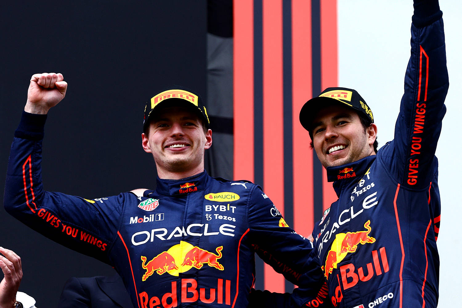 F1 桌布 壁紙 — 兩位紅牛一級方程式車手在頒獎台上高舉拳頭，面露喜悅，慶祝勝利。