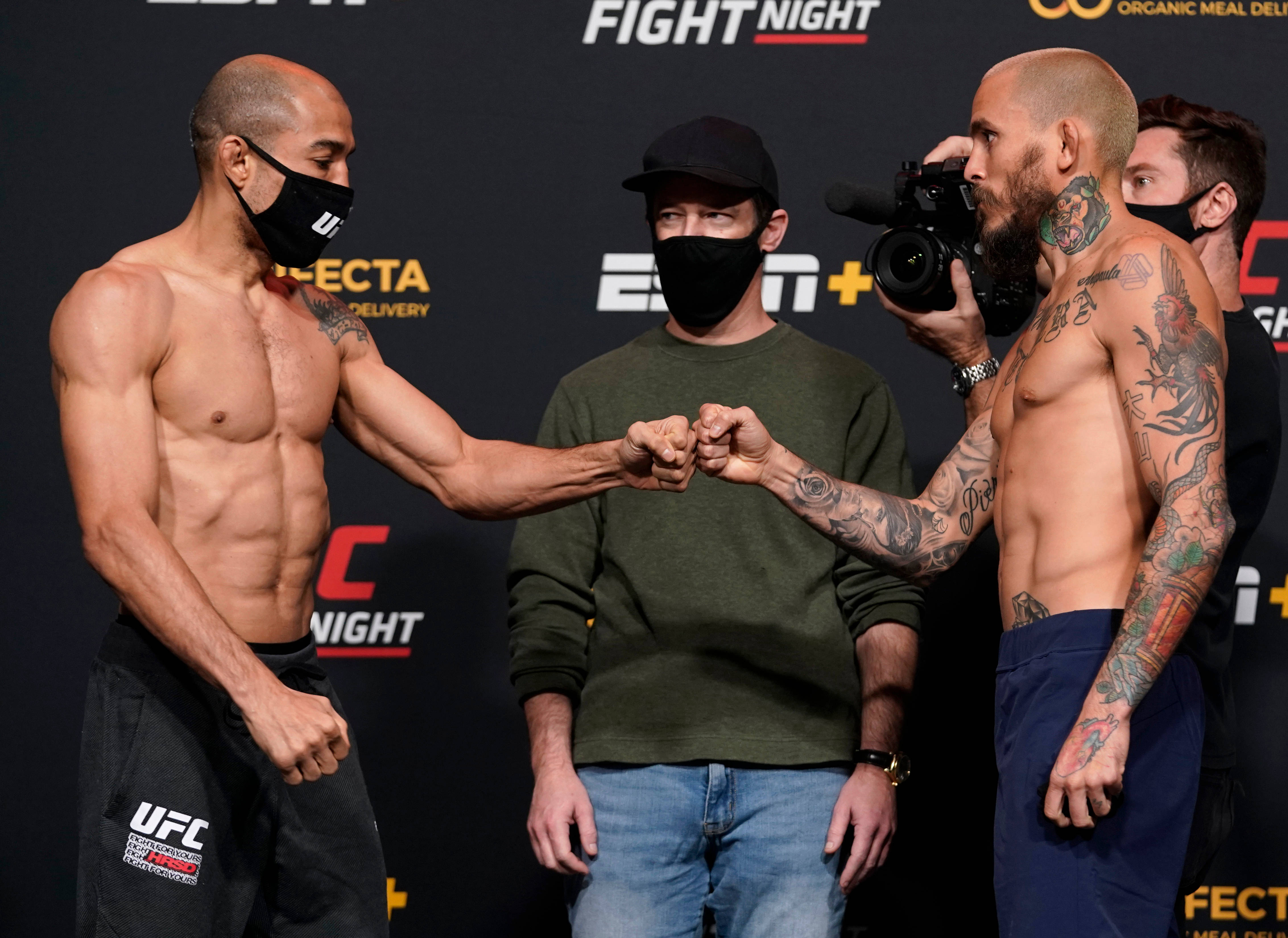 UFC 桌布 壁紙 — 兩位紋身UFC拳手在稱重活動中互相尊重地碰拳，背景有攝影師和贊助商標誌。