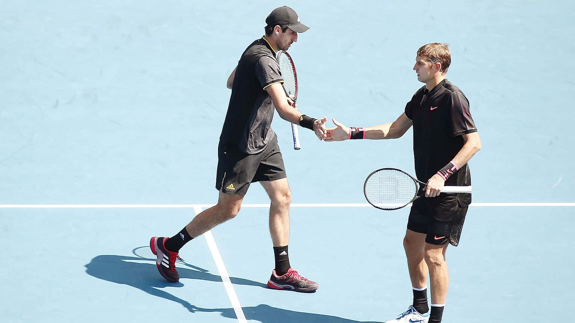Tennis 桌布 壁紙 — 兩位網球運動員在明亮的藍色球場上，在晴朗的日光下握手。