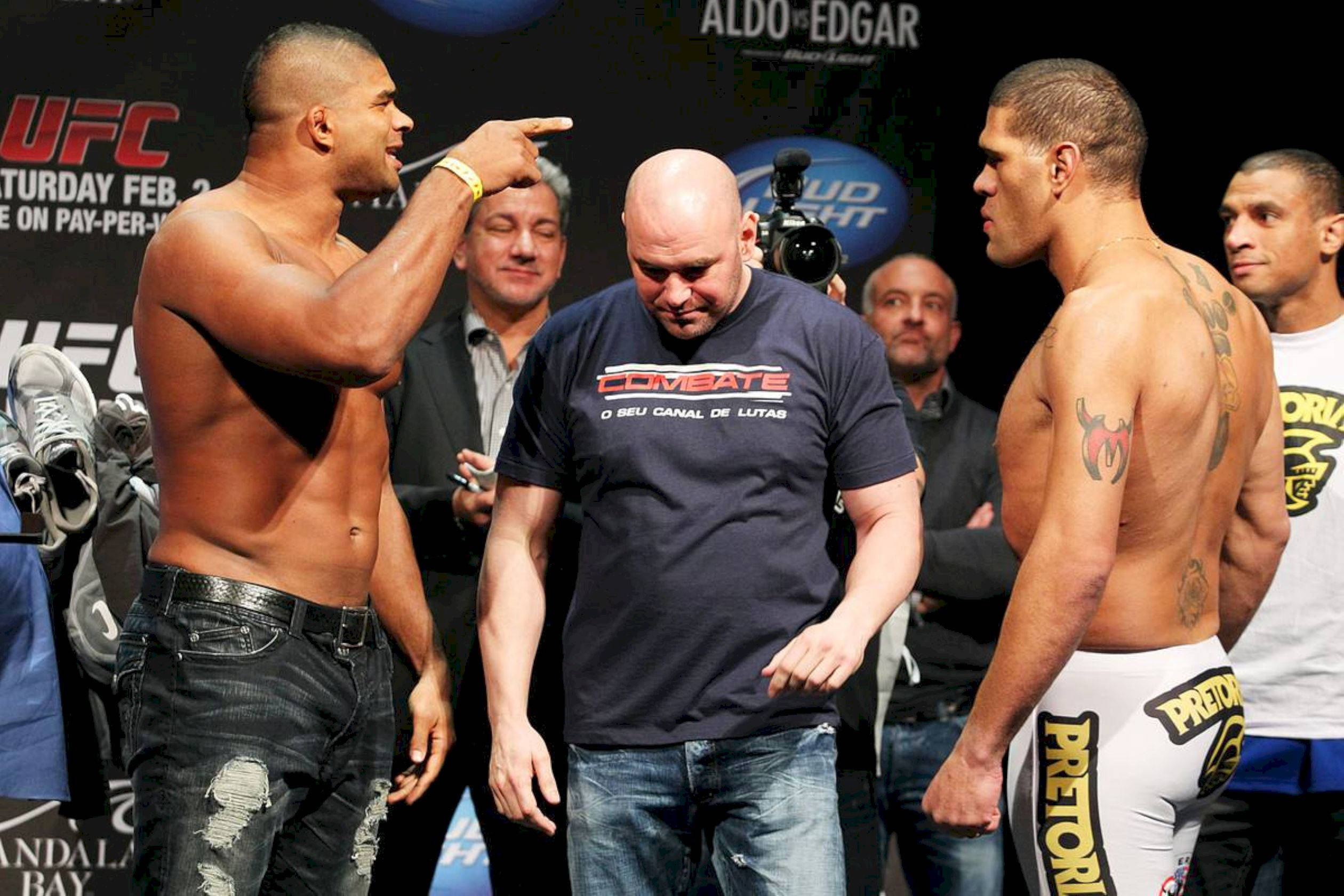 UFC 桌布 壁紙 — 兩位肌肉發達的UFC拳手在稱重活動中對峙，中間有一位光頭官員，背景是人群。