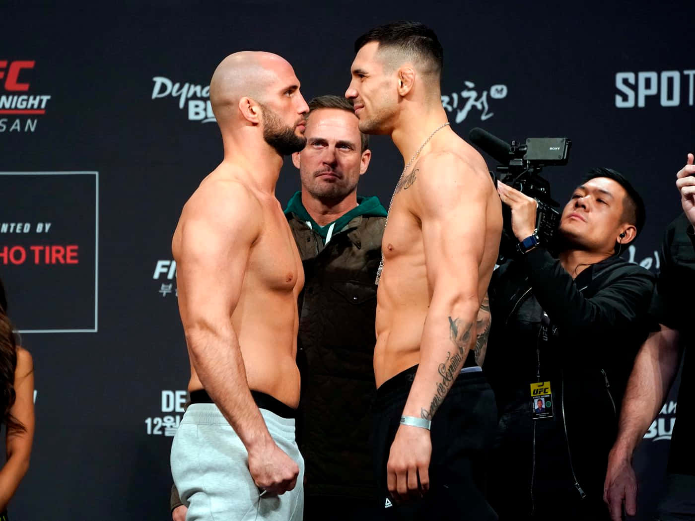 MMA 桌布 壁紙 — 兩位肌肉發達的UFC拳手在稱重活動中激烈對峙，周圍有相機和官員。