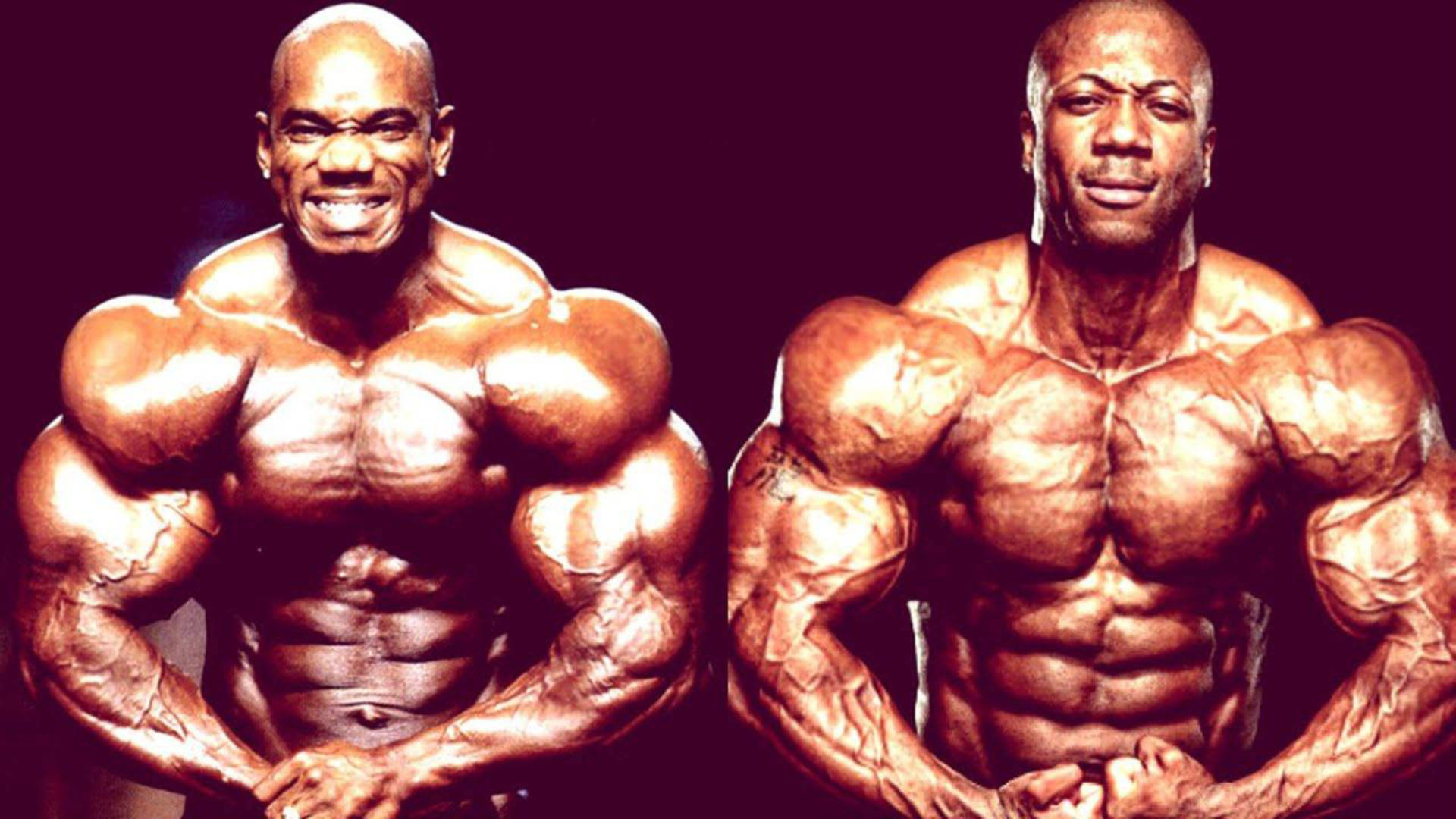 flex wheeler 桌布 壁紙 — 兩位肌肉發達的健美運動員在戲劇性燈光下，以深色背景襯托，展示清晰的腹肌和鼓起的二頭肌。