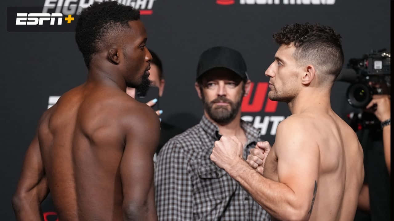 MMA 桌布 壁紙 — 兩位肌肉發達的拳手在UFC過磅時激烈對峙，周圍閃光燈不斷。