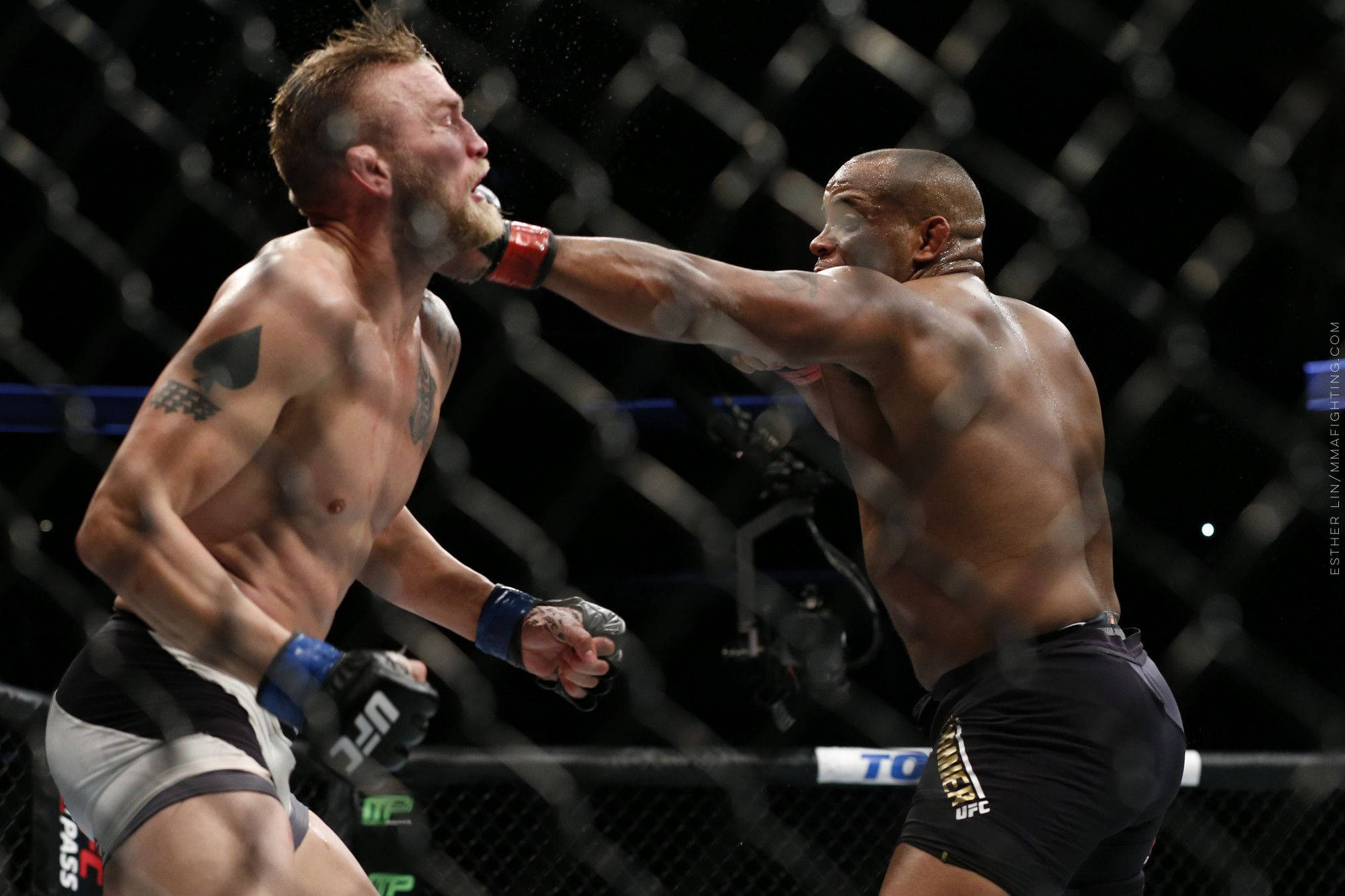 UFC 桌布 壁紙 — 兩位肌肉發達的拳手在明亮的場館燈光下，以鐵絲網圍欄為背景，進行激烈的MMA對決。