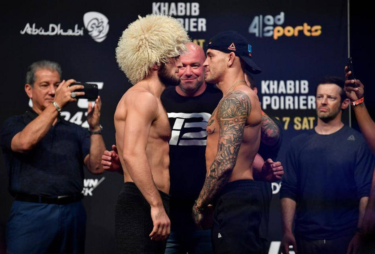 UFC 桌布 壁紙 — 兩位肌肉發達的拳手在稱重活動中對峙，其中一人戴著金色假髮，另一人身上有大量刺青。