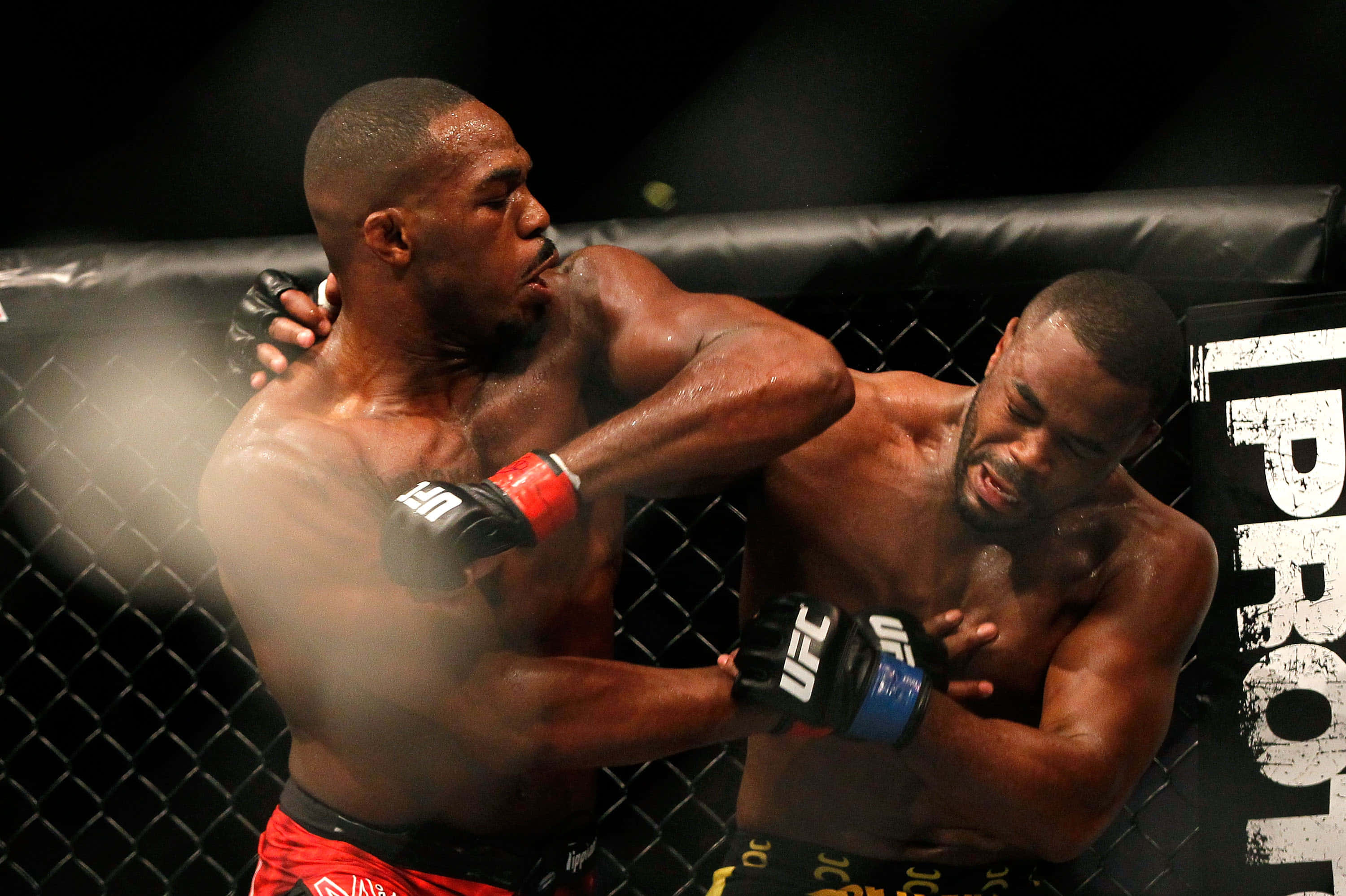 UFC 桌布 壁紙 — 兩位肌肉發達的拳手在籠中激烈交鋒，其中一人在激烈的MMA比賽中向對手面部重擊一拳。