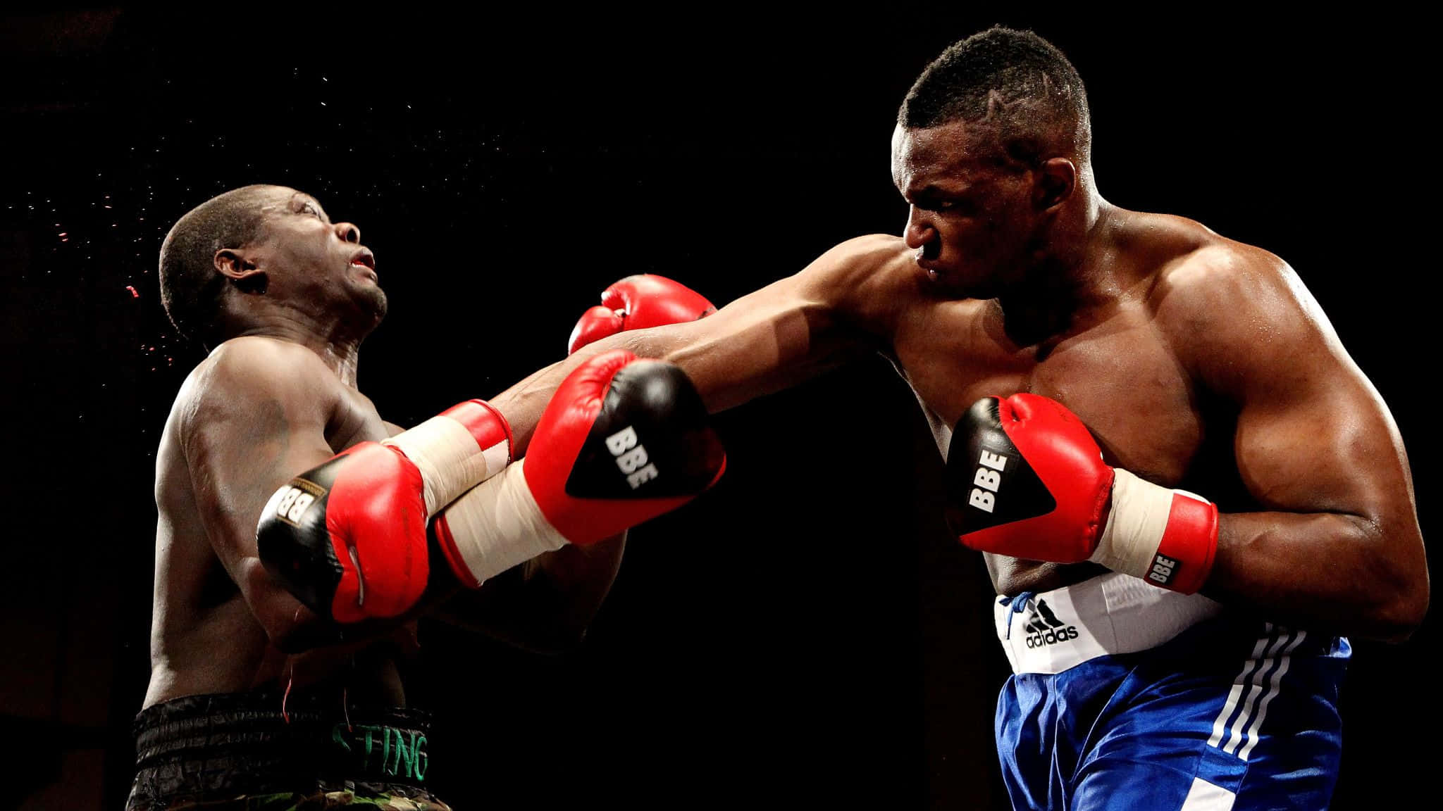 Boxing 桌布 壁紙 — 兩位肌肉發達的拳擊手在戲劇性的擂台上碰撞，紅色手套和汗水在黑色背景下飛濺。
