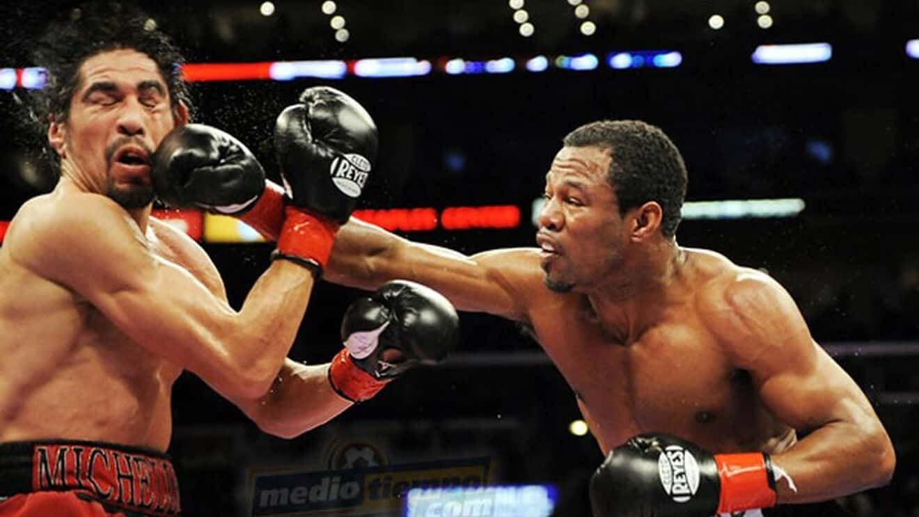 Boxing 桌布 壁紙 — 兩位肌肉發達的拳擊手在明亮的場館燈光下激烈交鋒，汗水飛濺，表情猙獰。