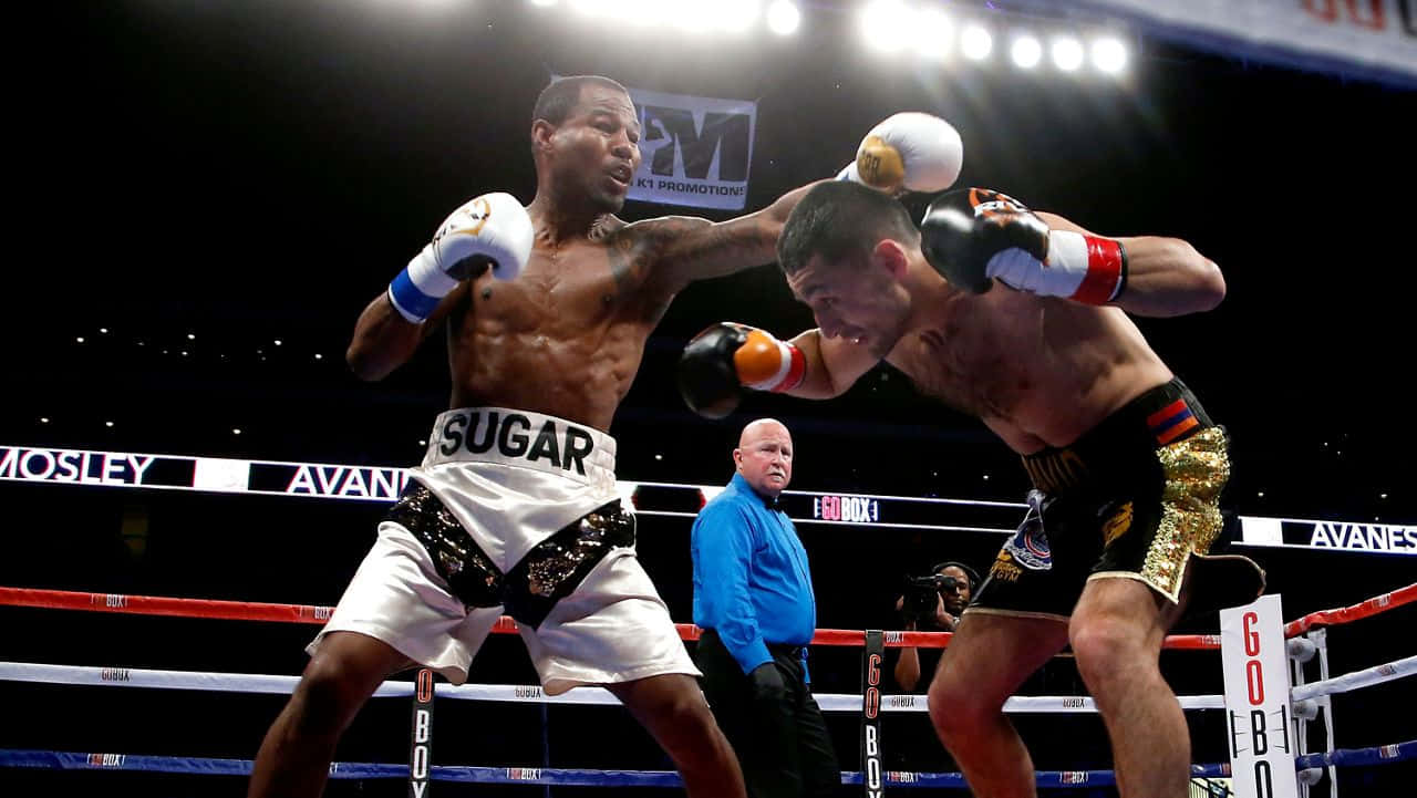 Boxing 桌布 壁紙 — 兩位肌肉發達的拳擊手在燈光明亮的擂台上交鋒，其中一人向對方頭部擊出強力一拳，裁判在旁緊密注視。