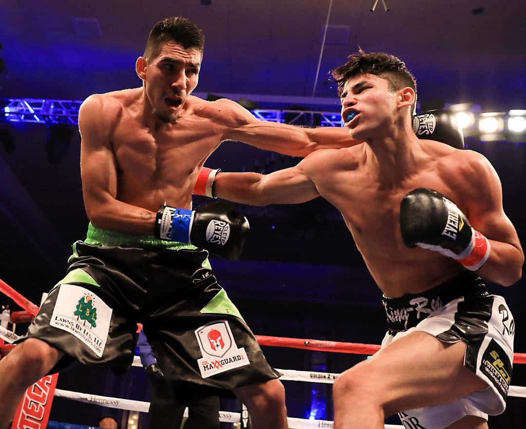 Boxing 桌布 壁紙 — 兩位肌肉發達的拳擊手在燈光明亮的擂台上交鋒，其中一人在激烈的比賽中向對方臉部擊出強力一拳。
