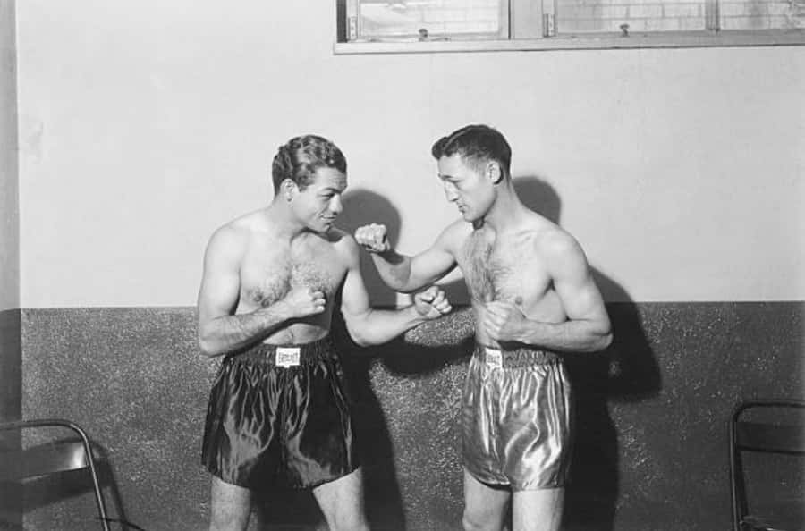 Fight 桌布 壁紙 — 兩位肌肉發達的拳擊手穿著復古緞面短褲，在光線對比強烈的簡陋健身房中激烈對打。