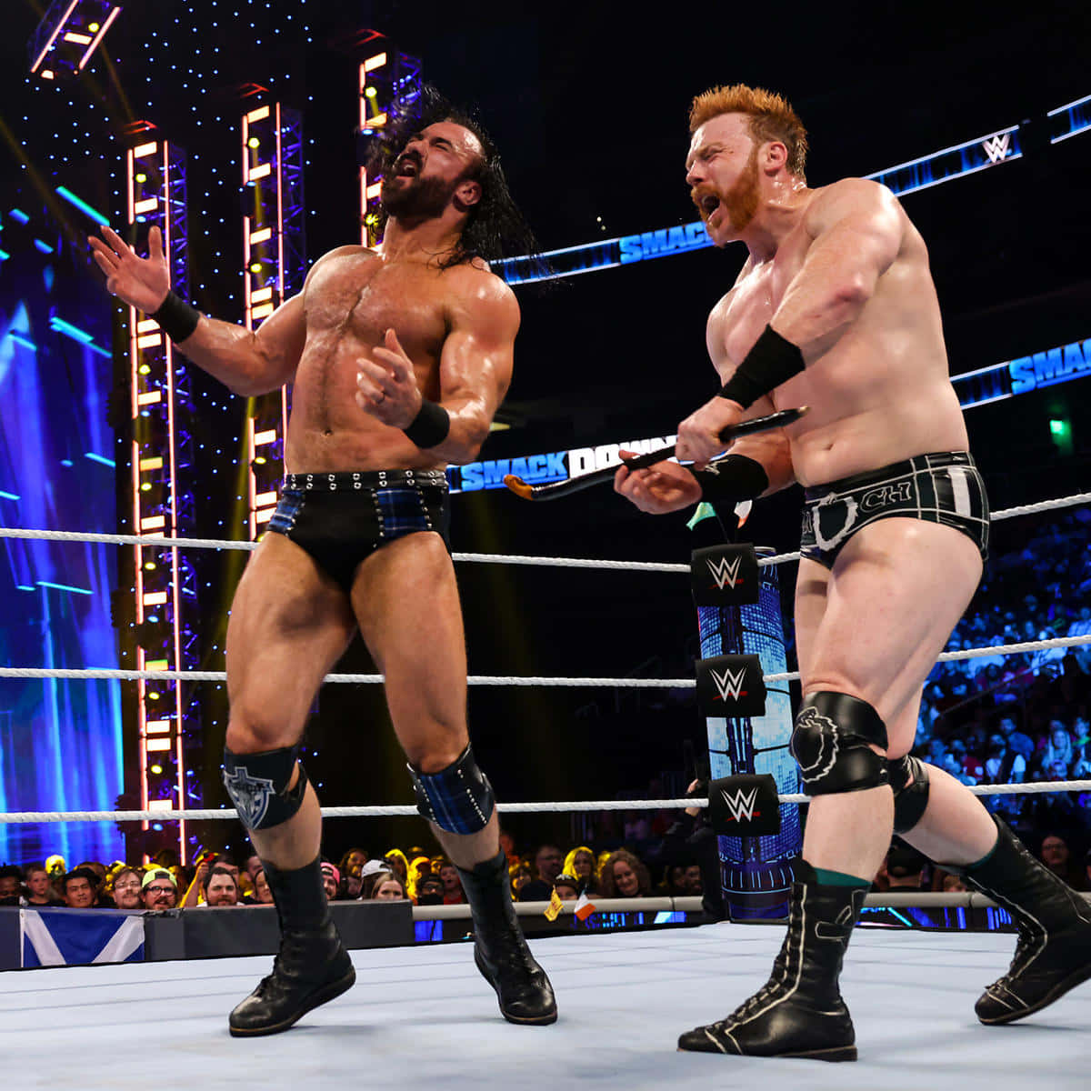 WWE 桌布 壁紙 — 兩位肌肉發達的摔角手在燈光明亮的擂台上對峙，一人手持椅子，另一人激烈地做手勢。
