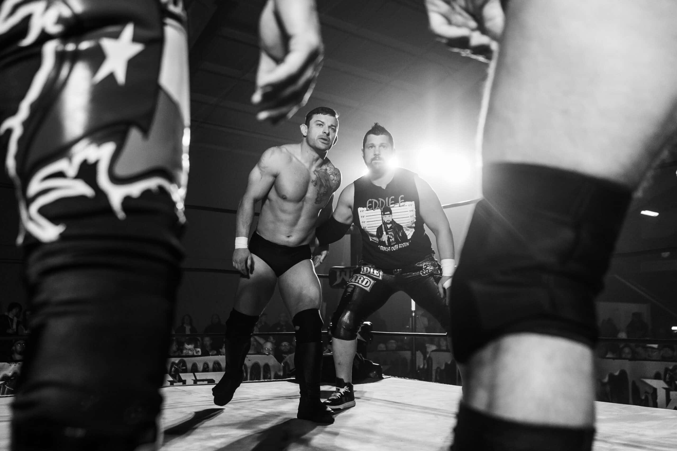WWE 桌布 壁紙 — 兩位肌肉發達的摔角手在燈光昏暗的擂台上對峙，背景有戲劇性的聚光燈和模糊的觀眾。