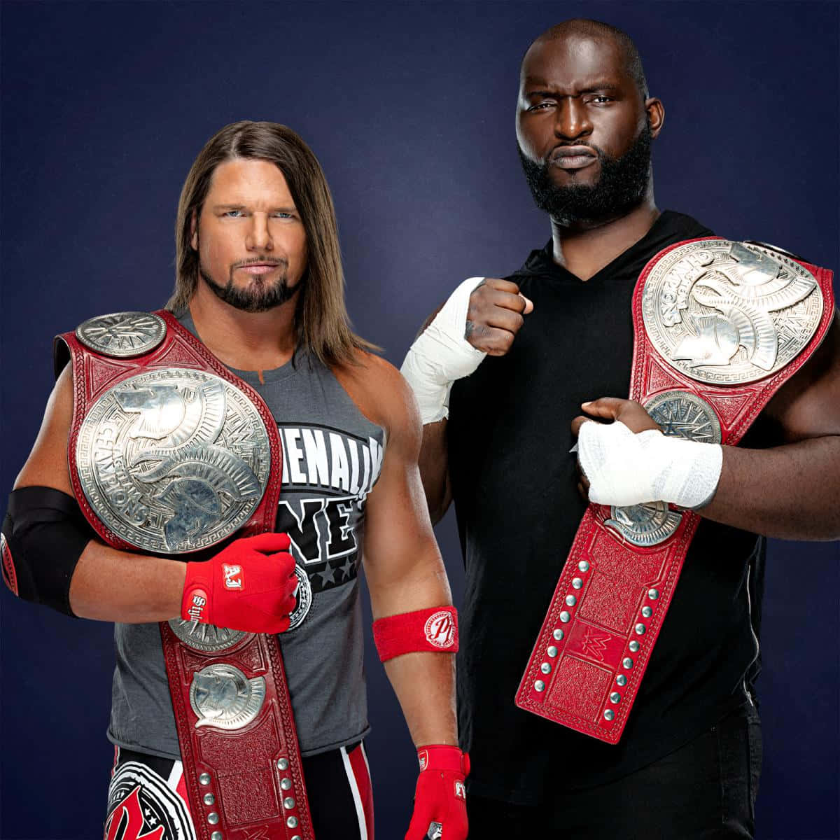 WWE 桌布 壁紙 — 兩位肌肉發達的摔角手自信地擺姿勢，手持冠軍腰帶，背景為深藍色攝影棚。