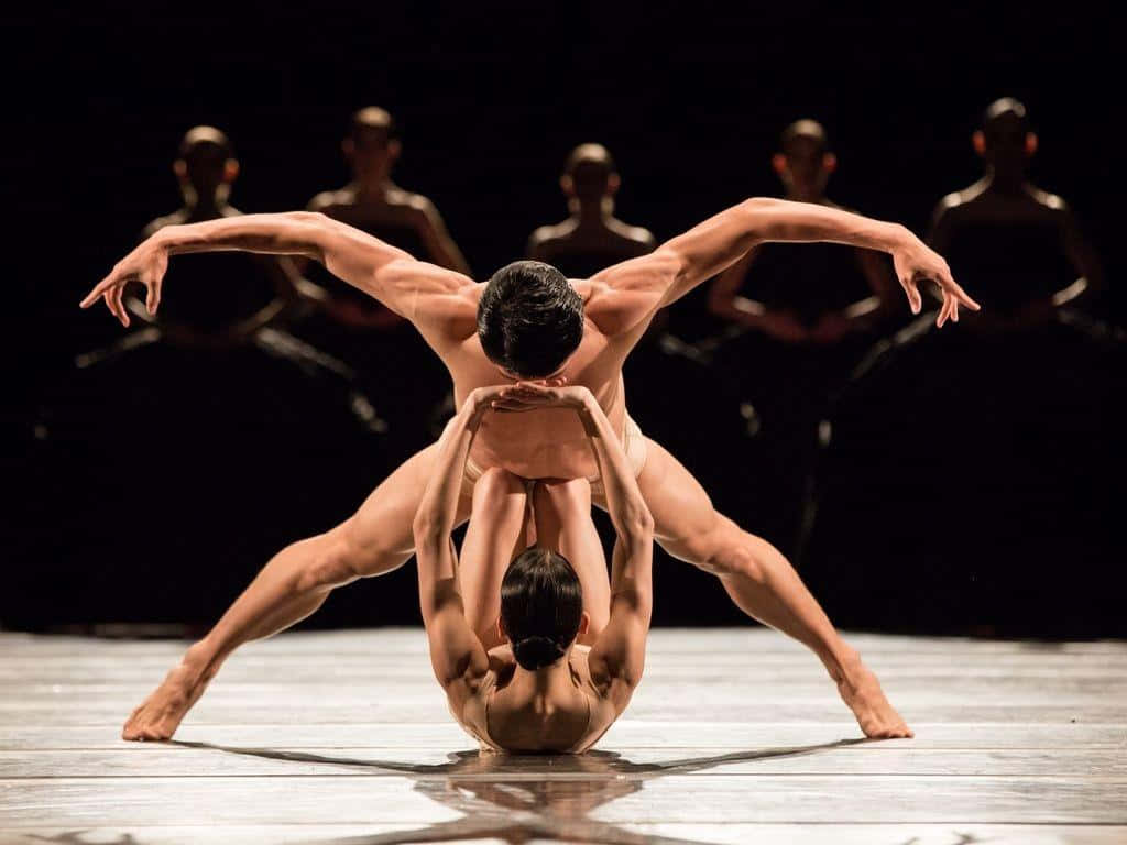 Ballet 桌布 壁紙 — 兩位舞者在舞台上伸展雙臂形成對稱姿勢，其他人則在他們身後以剪影觀看。