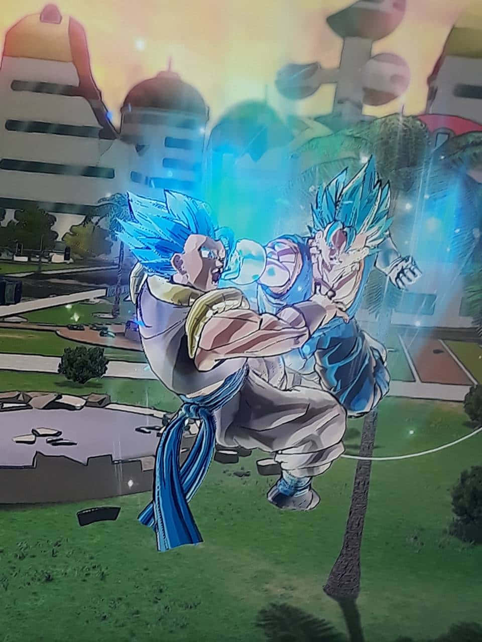Gogeta And Vegito 桌布 壁紙 — 兩位藍髮動漫戰士在夕陽下的城市景觀上空，於發光的能量爆發中交鋒。