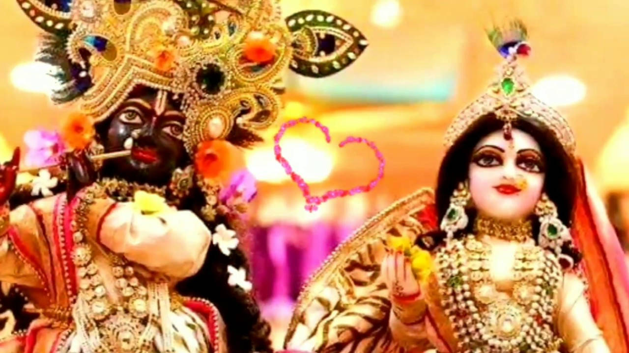 Krishna Janmashtami 桌布 壁紙 — 兩位裝飾華麗的印度教神祇，佩戴金飾和鮮豔服飾，彼此靠近站立，中間有一顆發光的心。