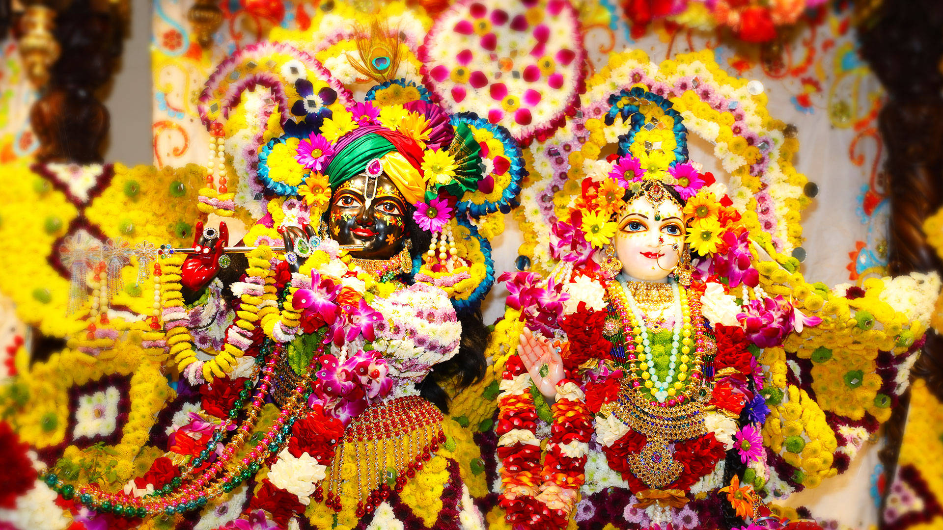 Hindu Temple 桌布 壁紙 — 兩位裝飾華麗的印度教神祇，戴著鮮豔的花冠和花環，站在色彩繽紛的花海中。