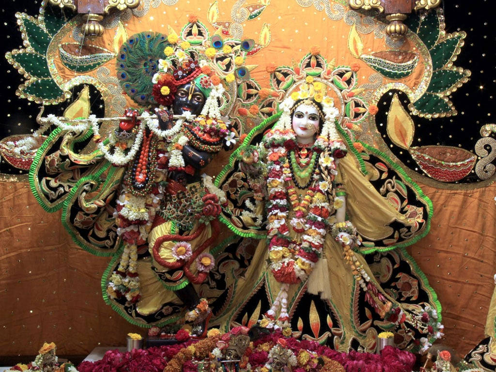 Hindu Temple 桌布 壁紙 — 兩位裝飾華麗的印度教神祇並排坐在鑲有寶石的華蓋下，披著鮮豔的花環和華麗的金色長袍。
