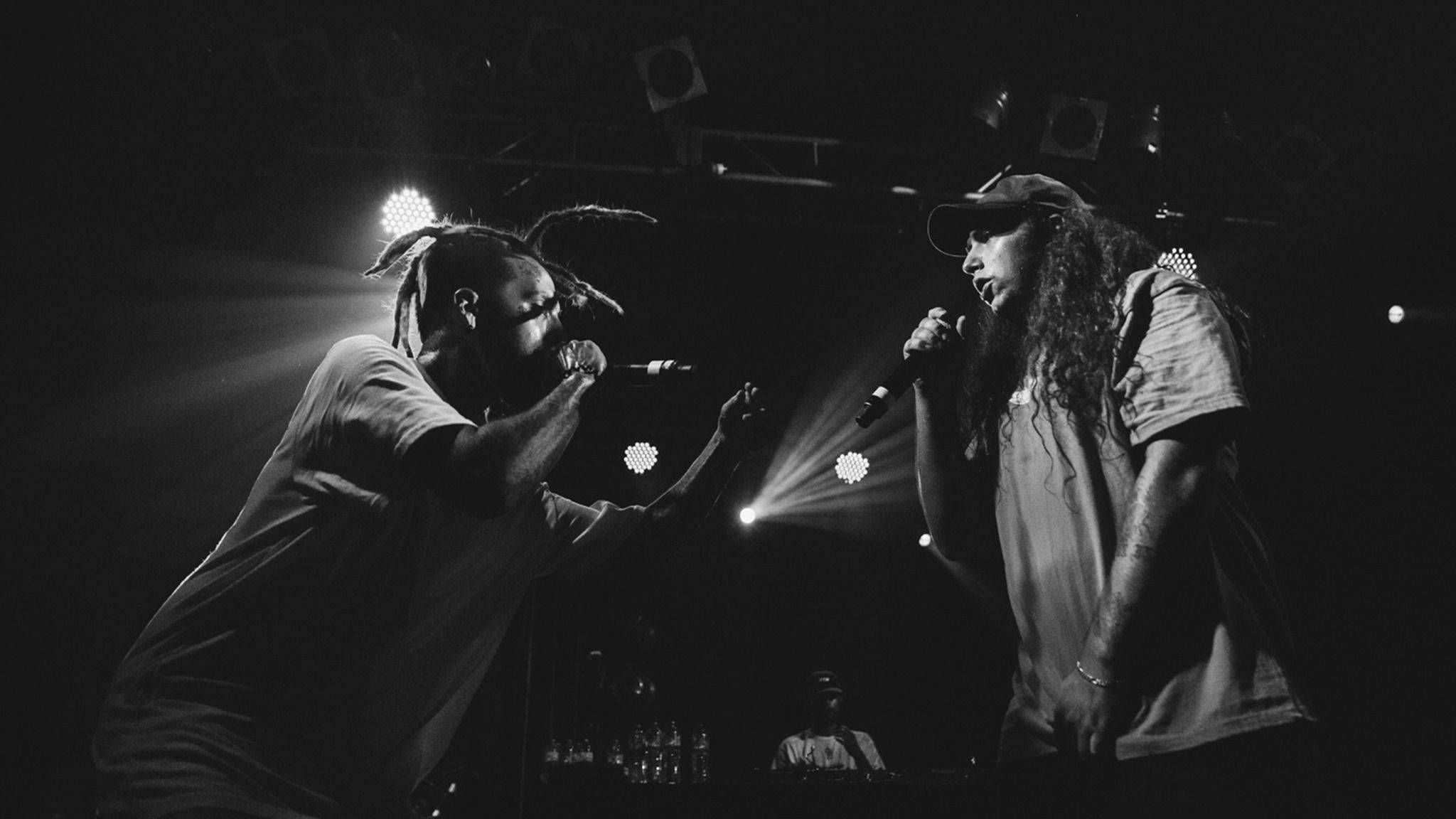 suicideboys 桌布 壁紙 — 兩位說唱歌手在戲劇性的舞台燈光下進行激烈對決的黑白演唱會照片。