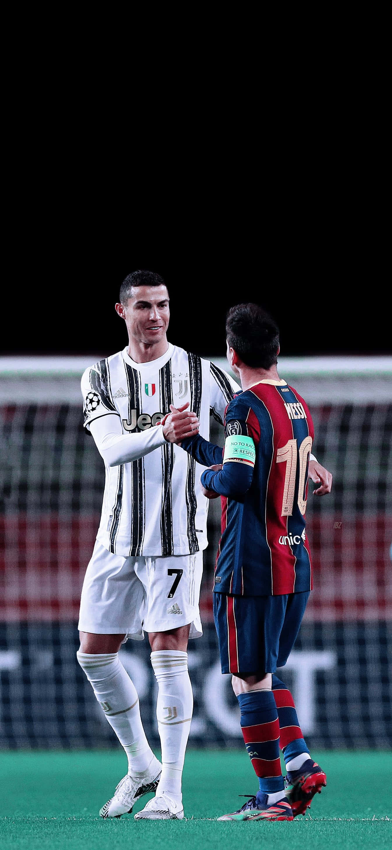 Messi And Ronaldo 4K 桌布 壁紙 — 兩位足球傳奇人物在球場燈光下，於昏暗的球場上握手，一位身穿尤文圖斯條紋球衣，另一位身穿巴塞隆納條紋球衣。