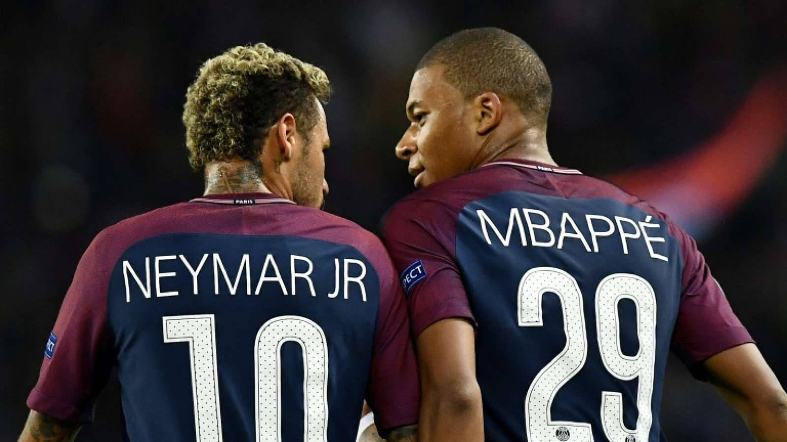 Kylian Mbappe 桌布 壁紙 — 兩位足球員內馬爾（Neymar Jr）和姆巴佩（Mbappé）身穿栗紅色球衣，在燈光昏暗的球場上專注交談。