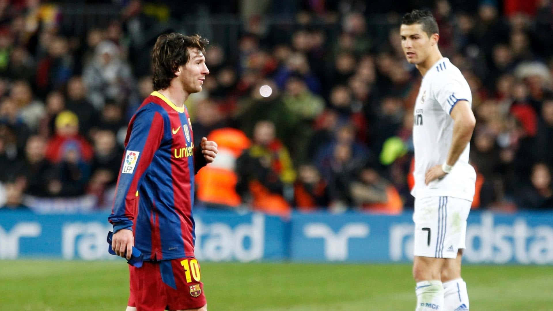 Messi And Ronaldo 4K 桌布 壁紙 — 兩位足球明星在明亮的燈光下於球場上對峙，背景是模糊的球迷。