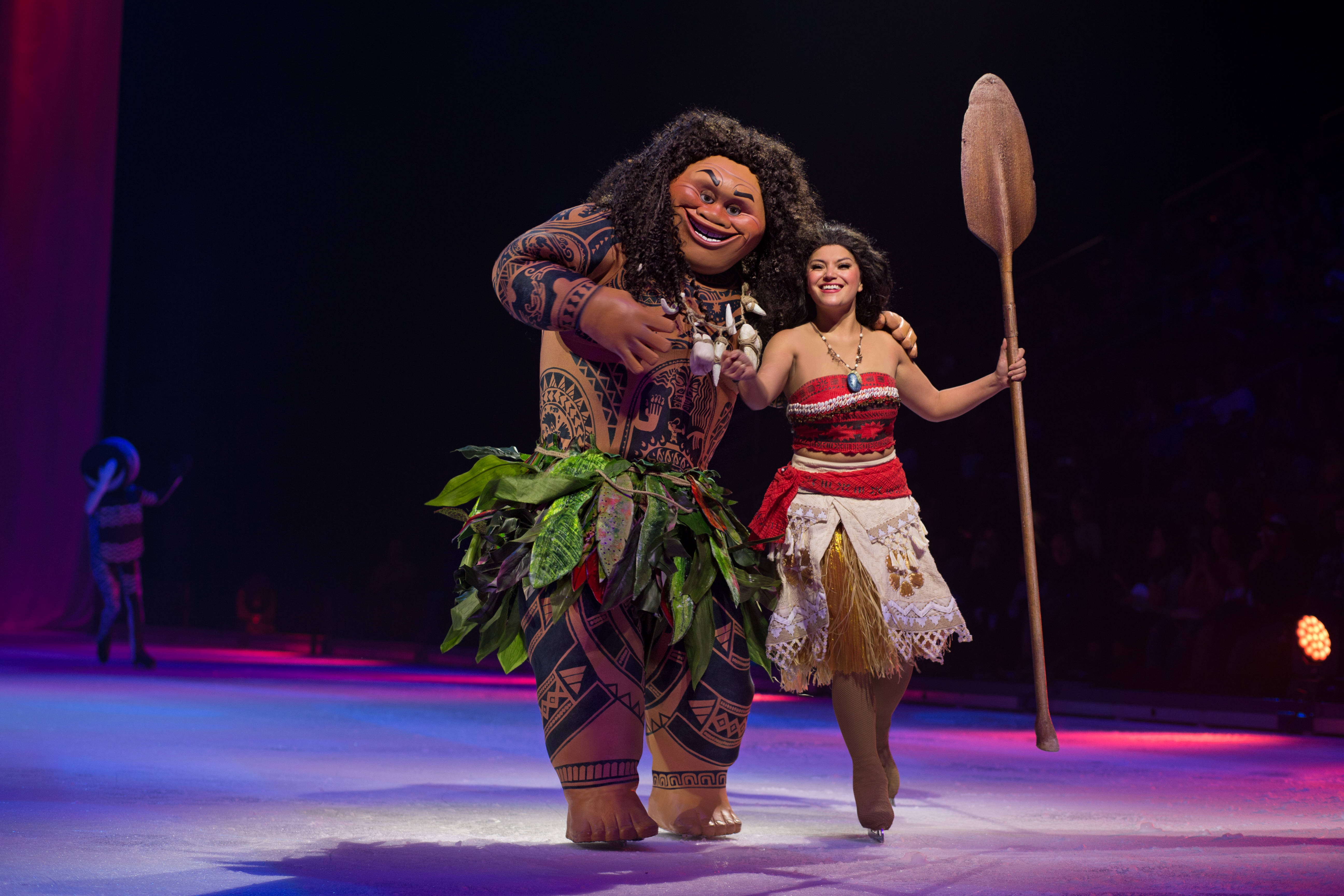 Maui 桌布 壁紙 — 兩位身穿 Moana 和 Maui 舞台服裝的表演者在紫色和藍色燈光的舞台上微笑擺姿勢。