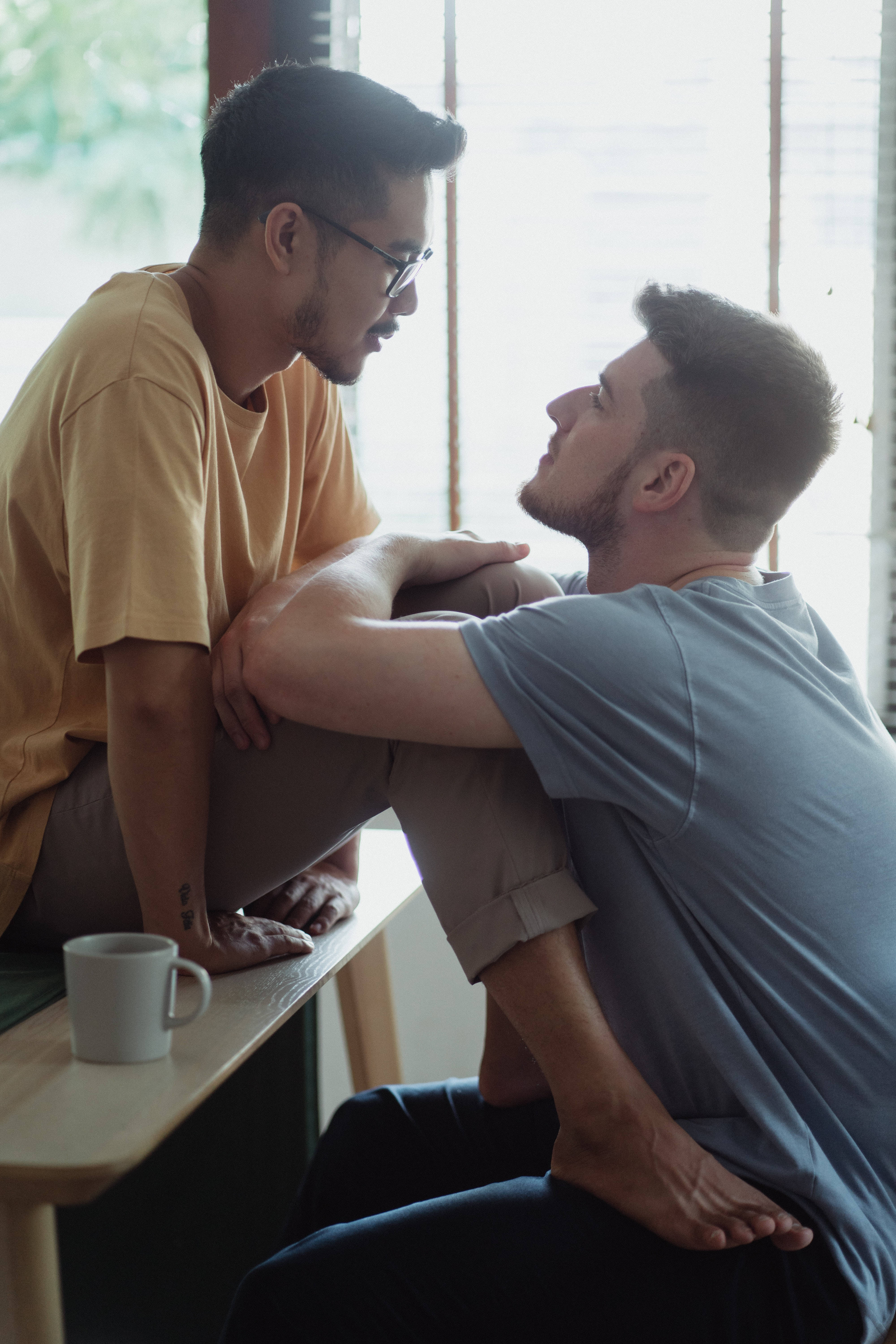 gay love 桌布 壁紙 — 兩位身穿休閒服的男士在明亮的咖啡館面對面坐著，進行親密的交談。