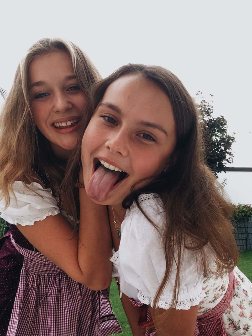 girls 桌布 壁紙 — 兩位身穿傳統Dirndl的年輕女性在戶外俏皮地擺姿勢，其中一個伸出舌頭，兩人都笑容燦爛。