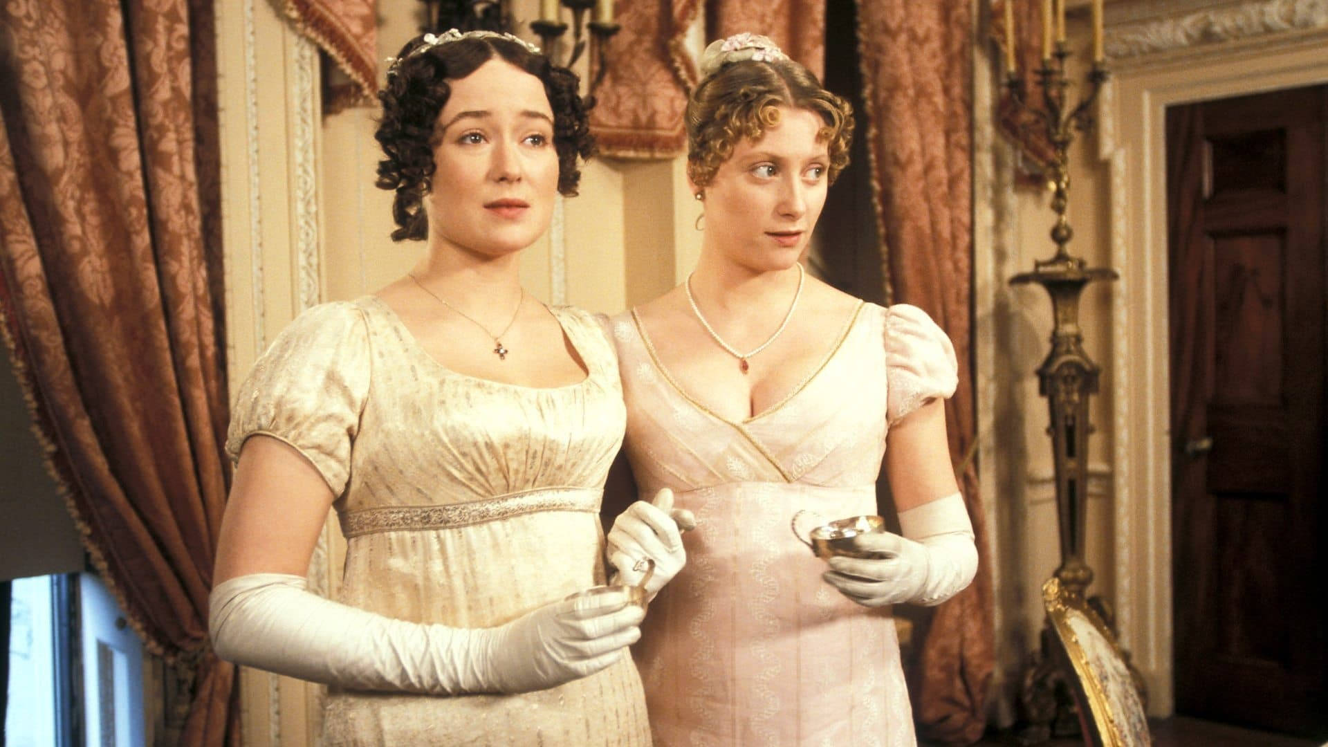 Pride And Prejudice 桌布 壁紙 — 兩位身穿優雅時代服飾的女性，在裝飾華麗的維多利亞時代客廳中手持茶杯。