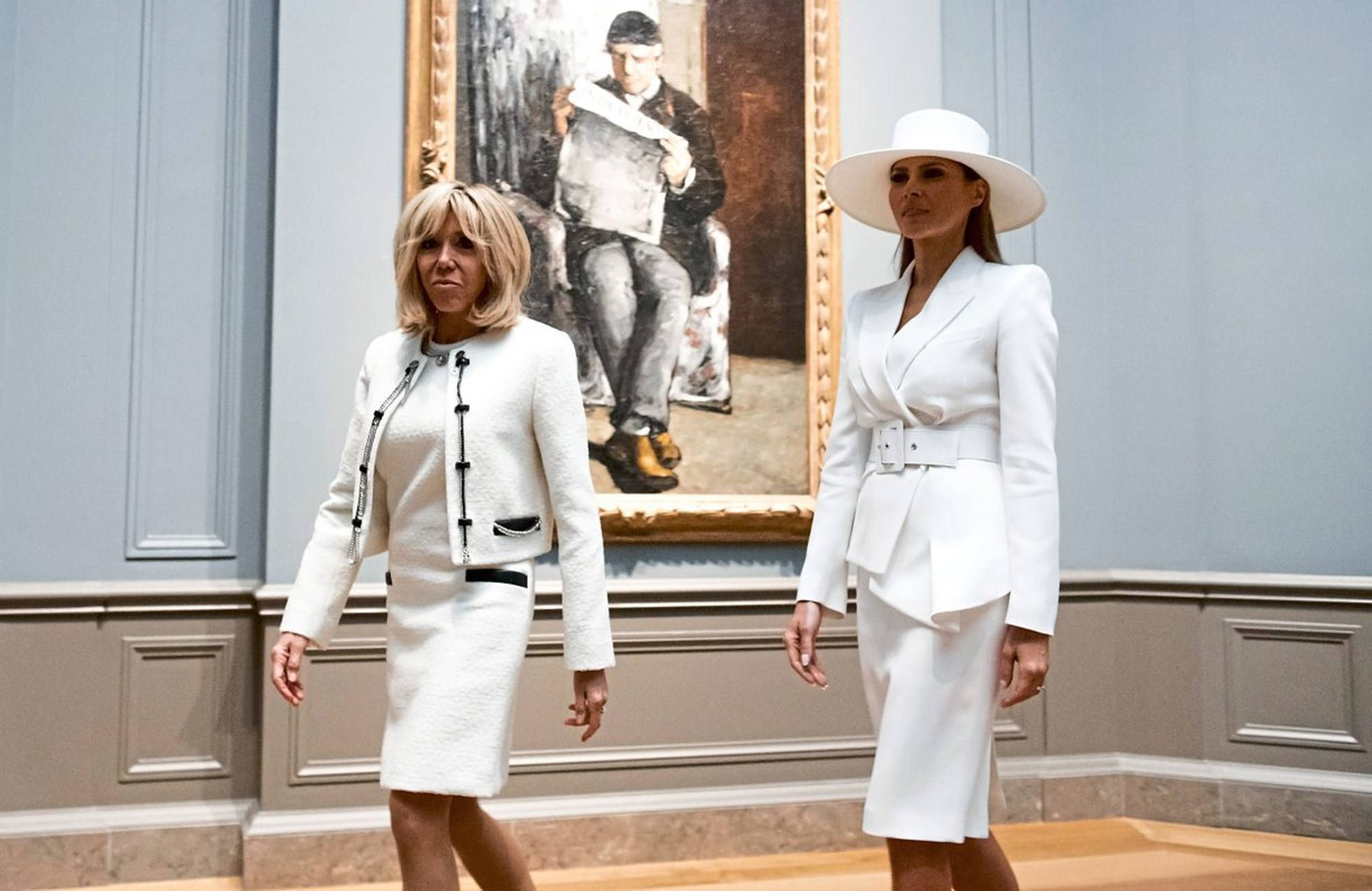 Melania 桌布 壁紙 — 兩位身穿優雅白色服裝的女性走過一個宏偉的畫廊，旁邊是一幅大型裱框畫作。