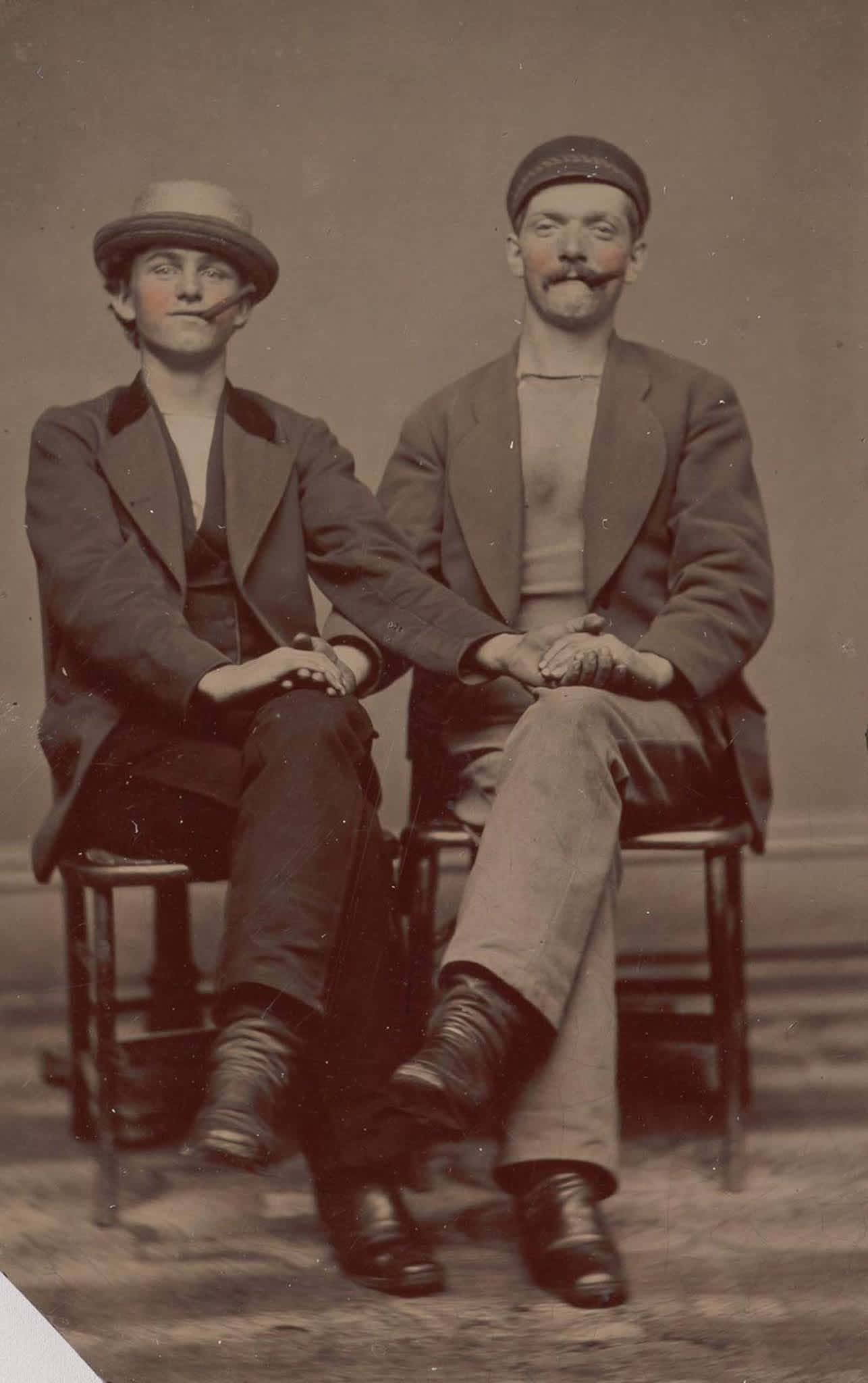 Victorian 桌布 壁紙 — 兩位身穿復古服裝的男士並排坐在凳子上，在復古色調的攝影棚肖像中牽手。