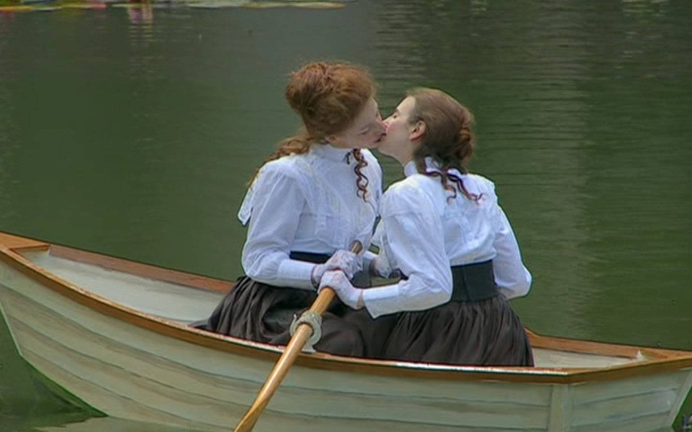 Kissing 桌布 壁紙 — 兩位身穿復古白襯衫和深色裙子的女性在平靜的綠色池塘上的木製划艇中溫柔地接吻。