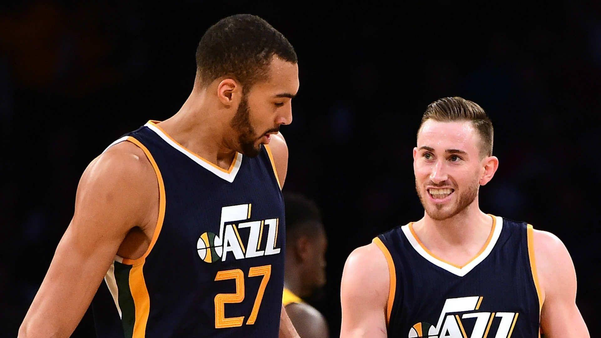 gordon hayward 桌布 壁紙 — 兩位身穿海軍藍配黃色點綴球衣的猶他爵士籃球運動員，在明亮的場館燈光下於比賽中分享一個時刻。